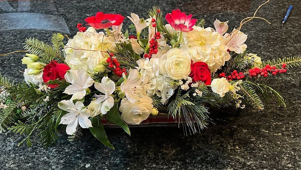 Floral centerpiece with white hydrangeas, red anemones, and greenery in a rectangular container.