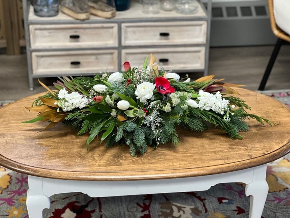 A floral arrangement with white flowers and greenery sits on a round, light brown coffee table.