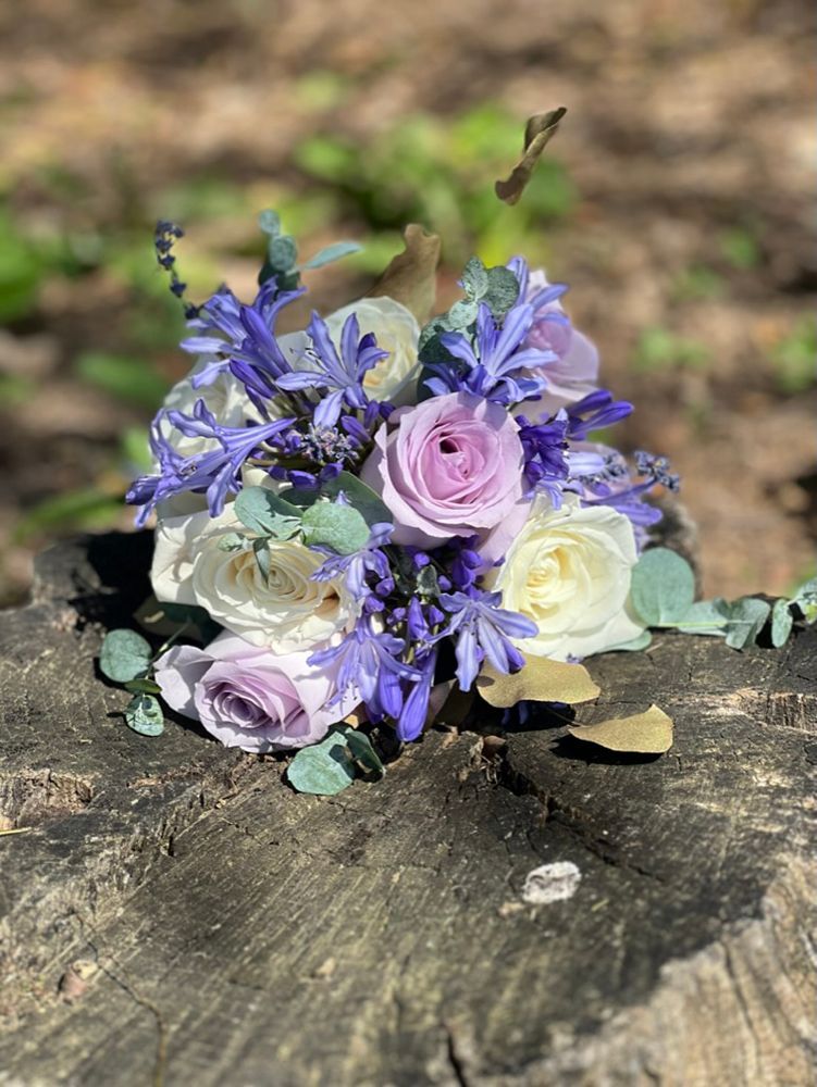 Bouquet of lavender, white, and purple roses and other flowers on a weathered wooden surface.