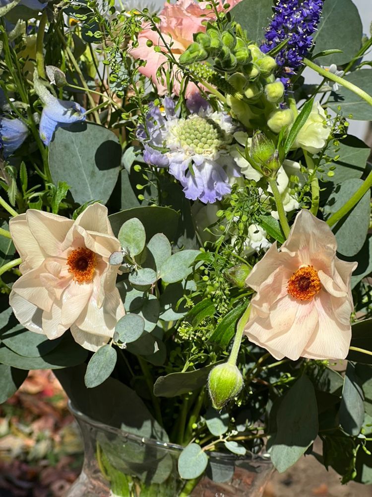 Close-up of a floral arrangement with peach poppies and eucalyptus, with other blooms in shades of pink, purple, and green.