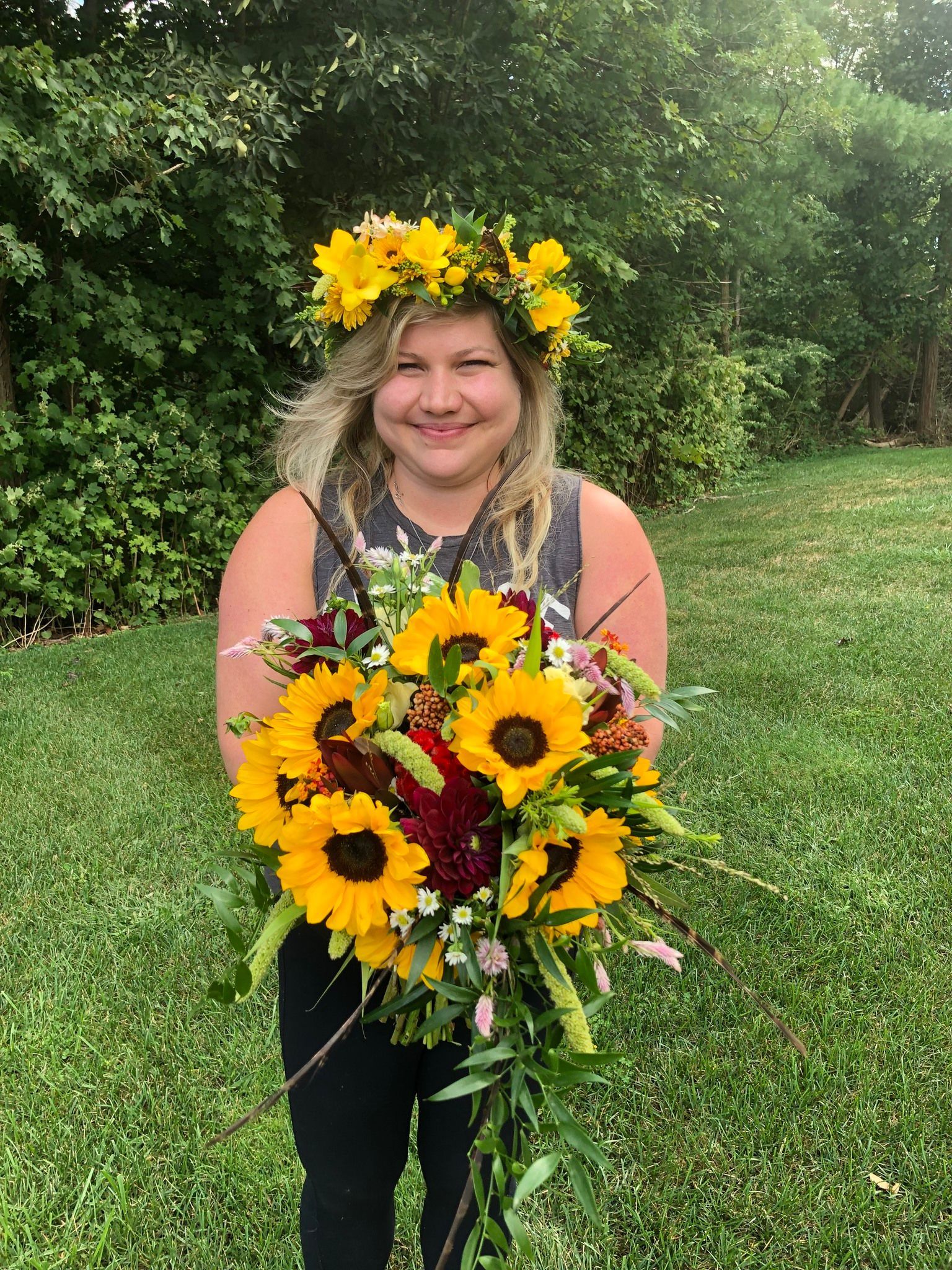 A woman wearing a flower crown is holding a bouquet of sunflowers.
