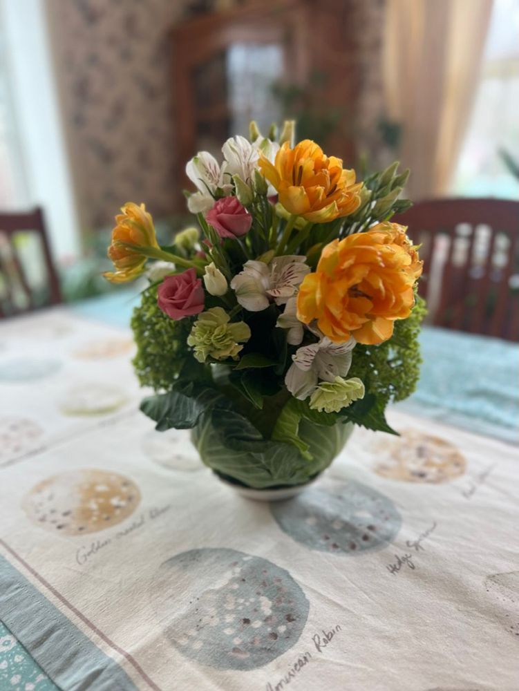 A floral centerpiece with orange tulips and white flowers, arranged in a cabbage base, on a table with a moon-themed tablecloth.