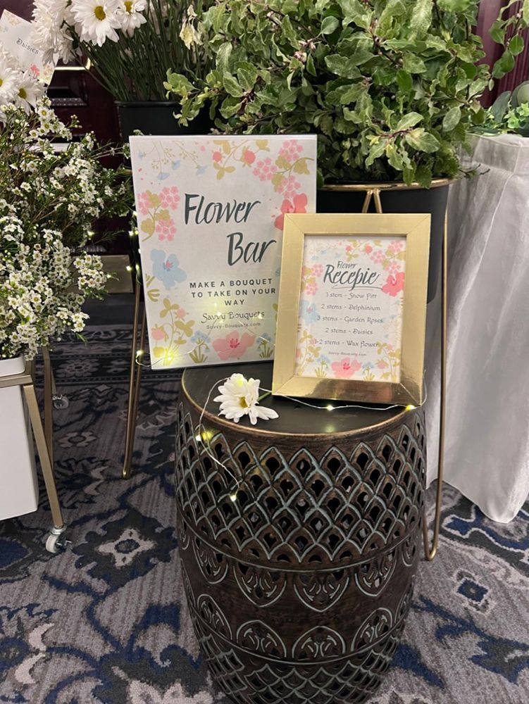Flower bar setup with signs on a decorative stool; a