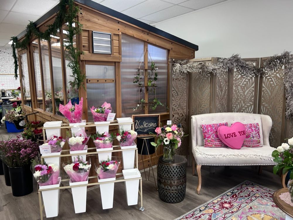Floral shop display featuring bouquets, a small greenhouse structure, a loveseat with a