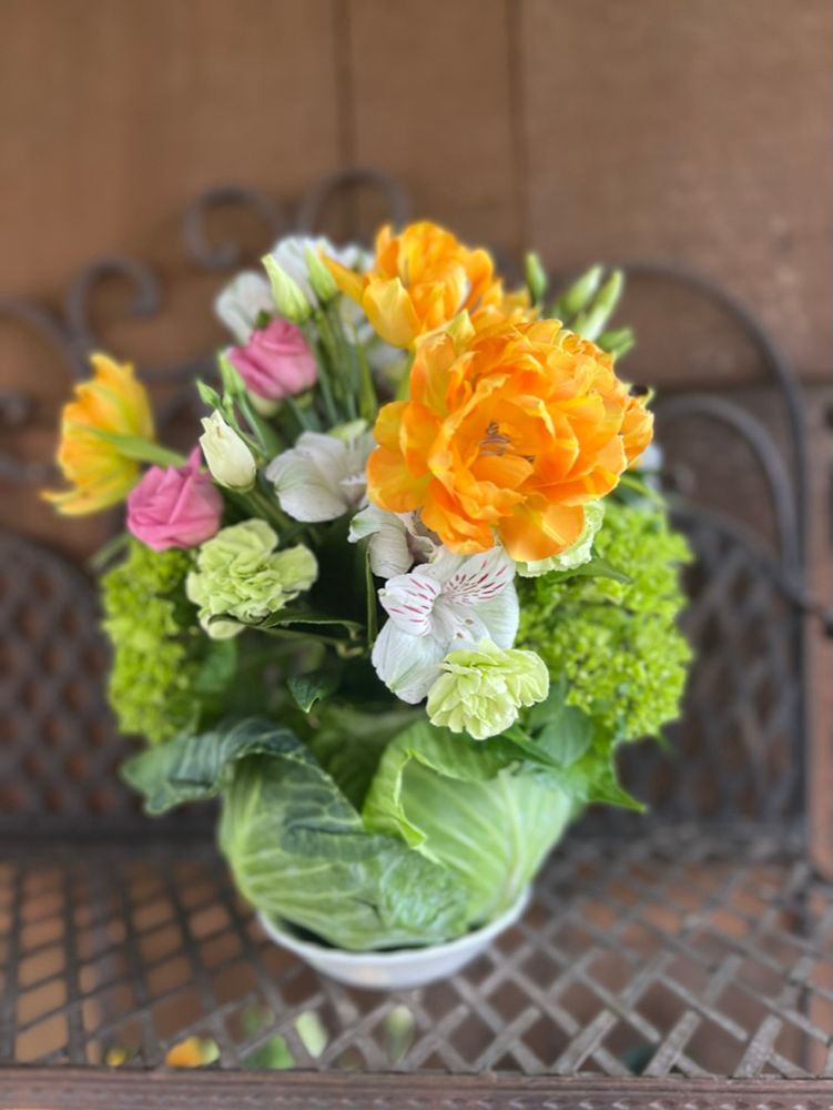 A floral arrangement featuring vibrant orange tulips and pink roses, arranged within a hollowed-out cabbage.
