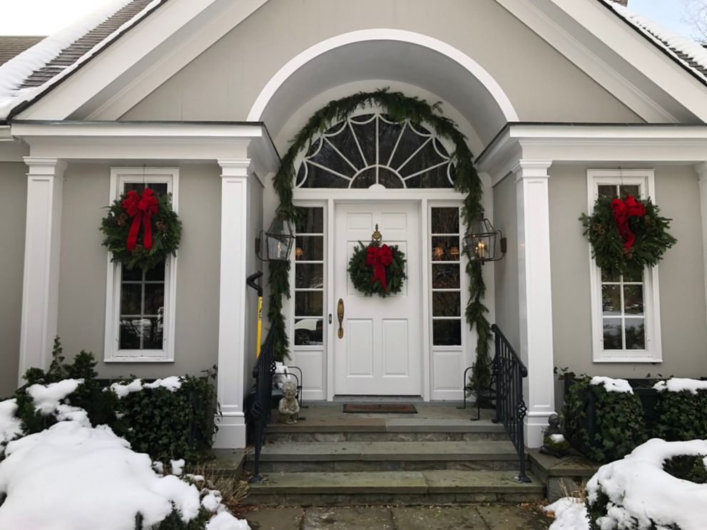 Snowy front entrance decorated for Christmas with wreaths and garland. White door and trim with gray exterior.