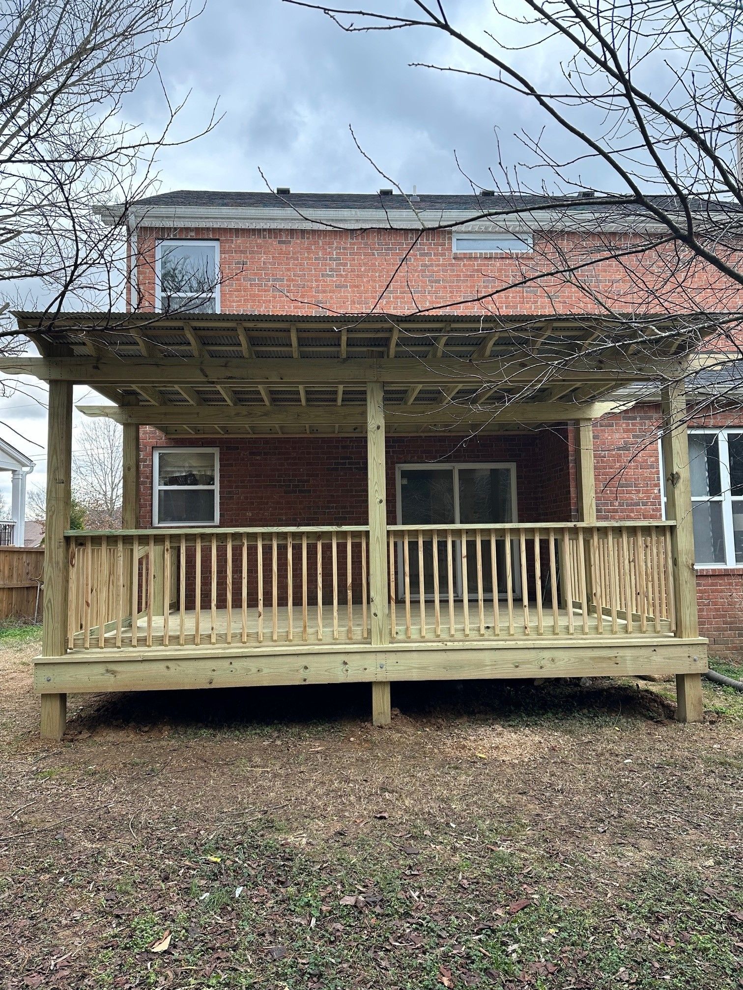 A wooden deck with a pergola is in front of a brick house