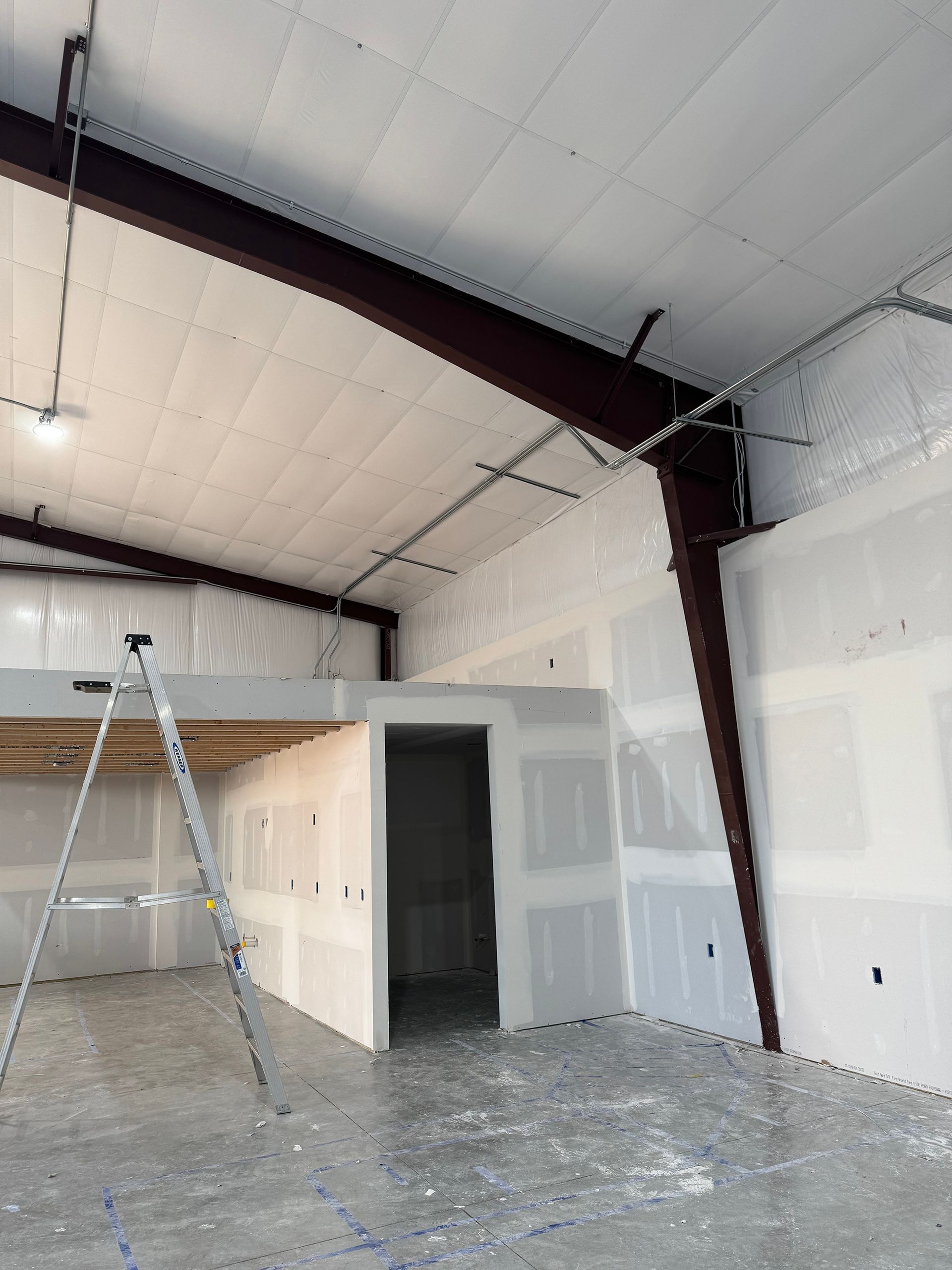 Construction of a commercial interior with exposed steel beams, drywall, and a concrete floor.