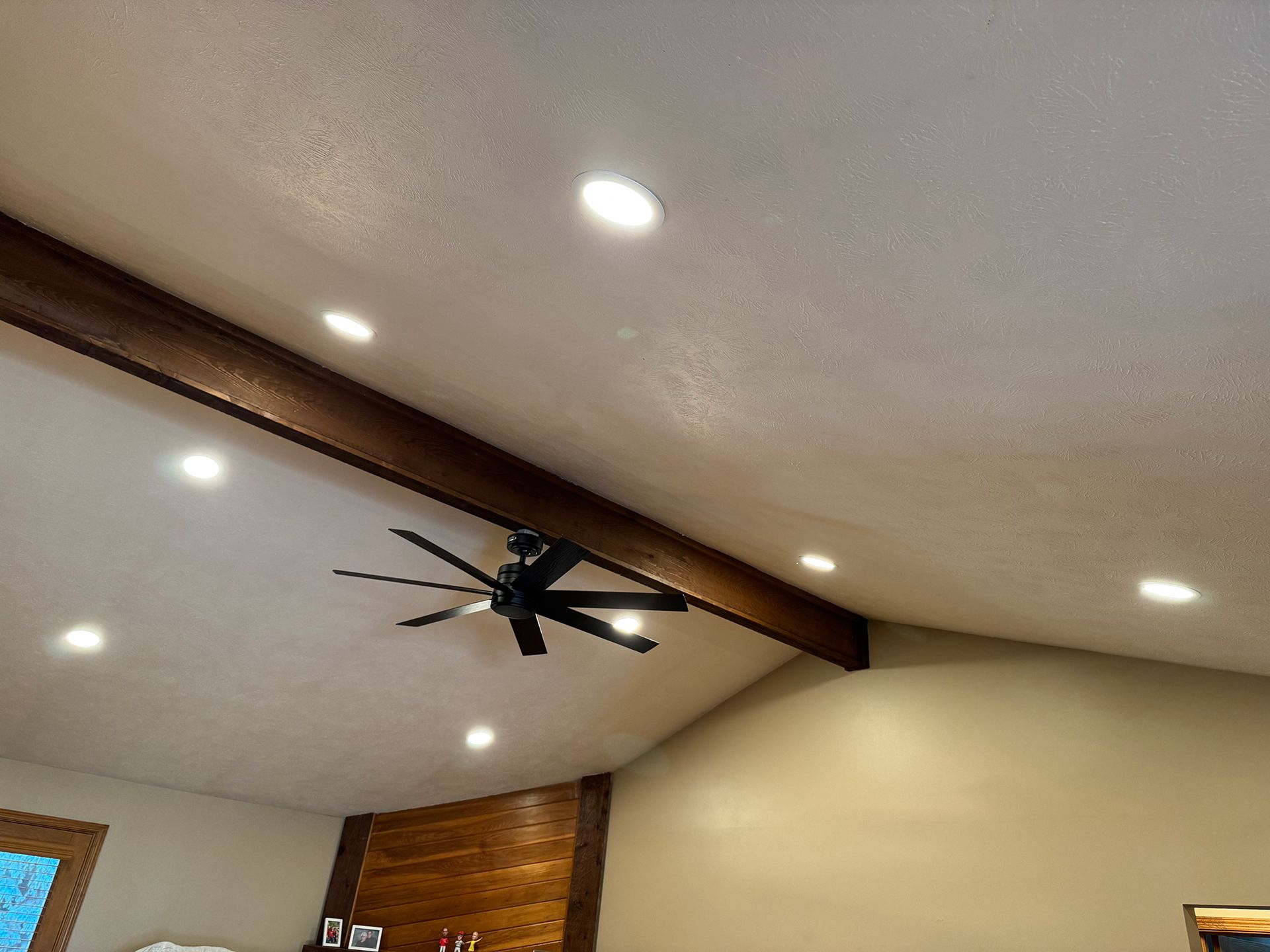 A vaulted ceiling with recessed lights, a dark wood beam, and a black ceiling fan.