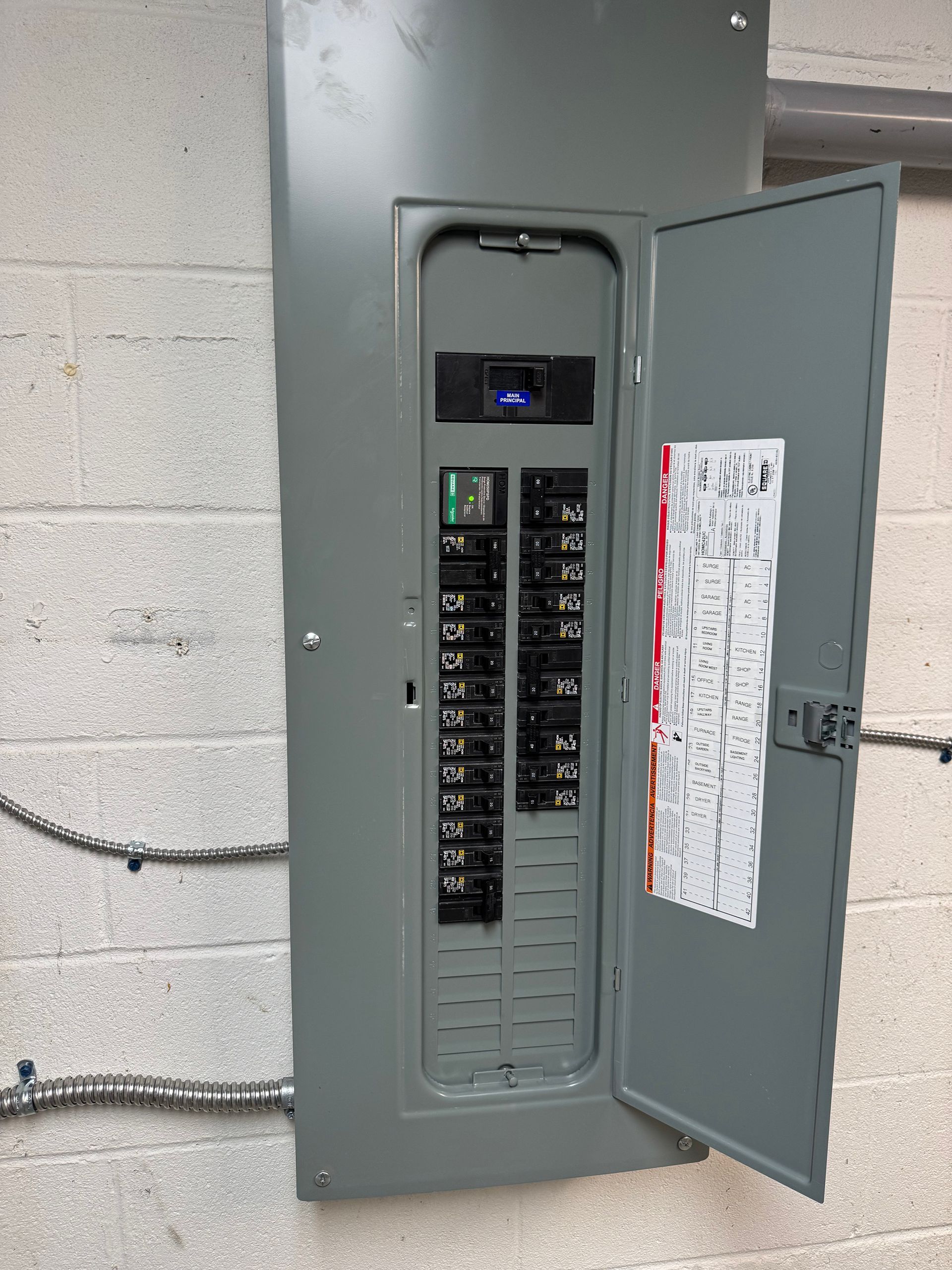 Electrical panel, gray metal box mounted on a white brick wall, door open showing circuit breakers.