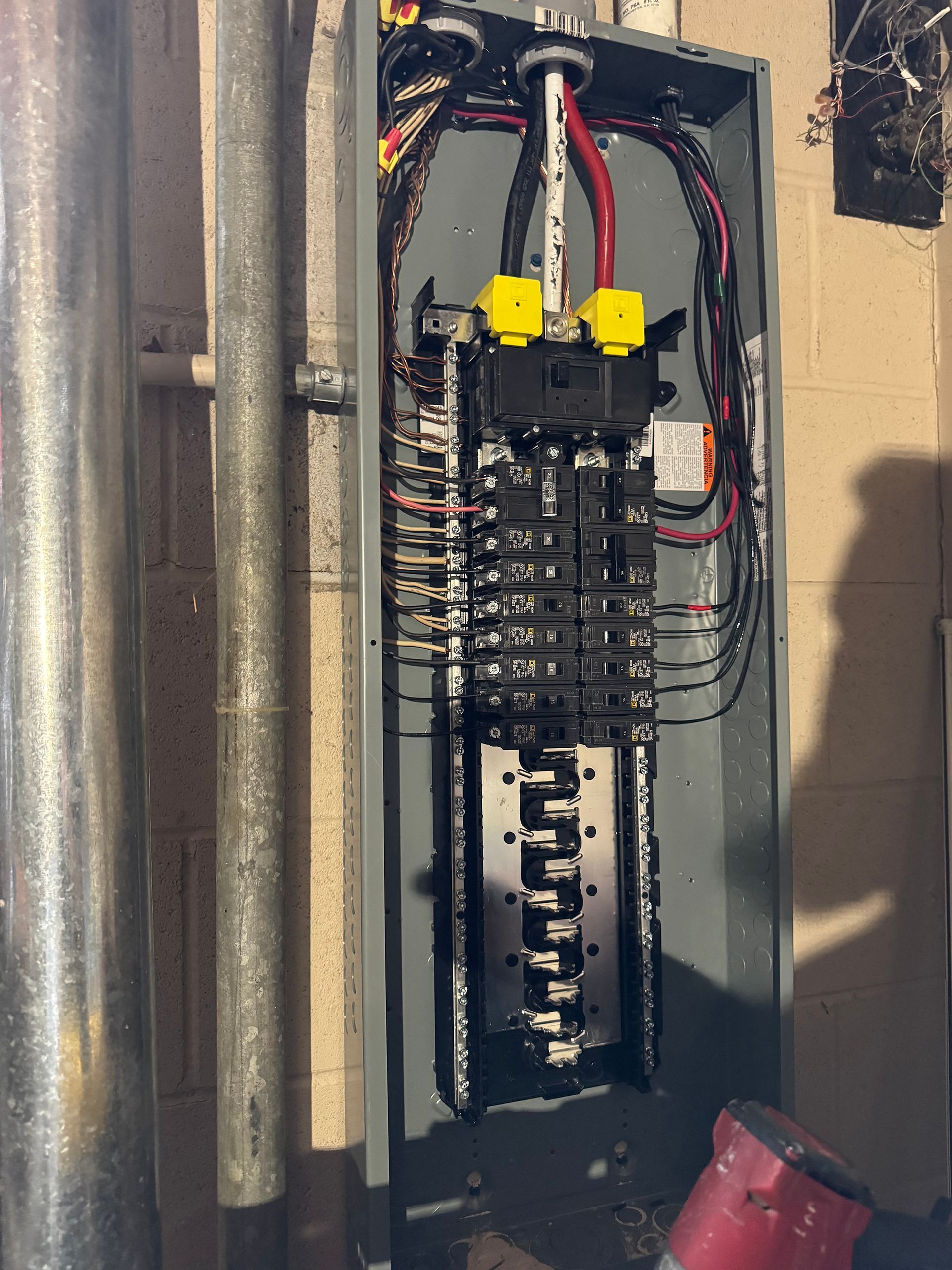 Electrical panel with breakers and wiring inside a metal enclosure, installed on a concrete wall.
