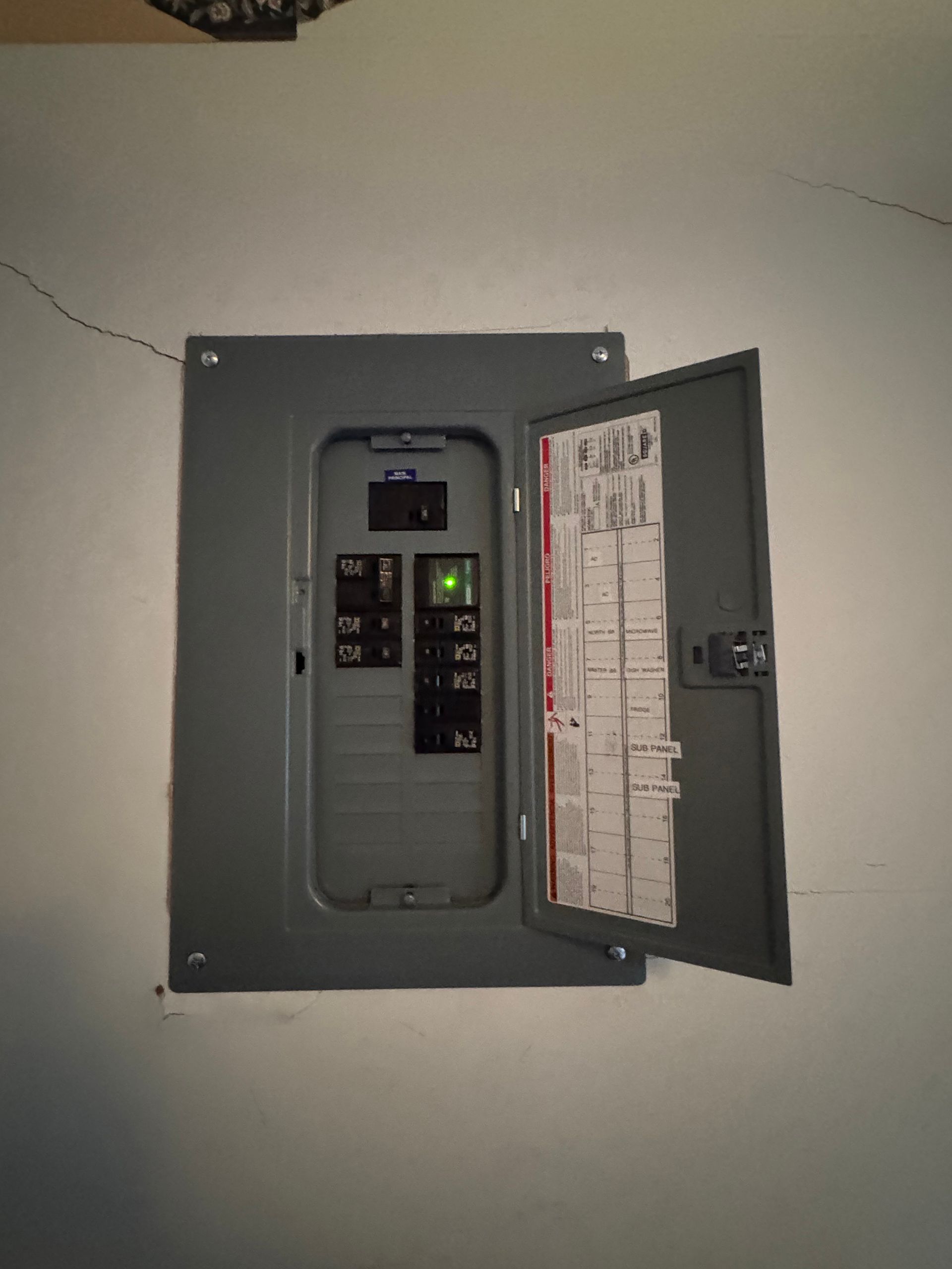 Gray electrical panel mounted on a white wall, door open, with circuit breakers visible.