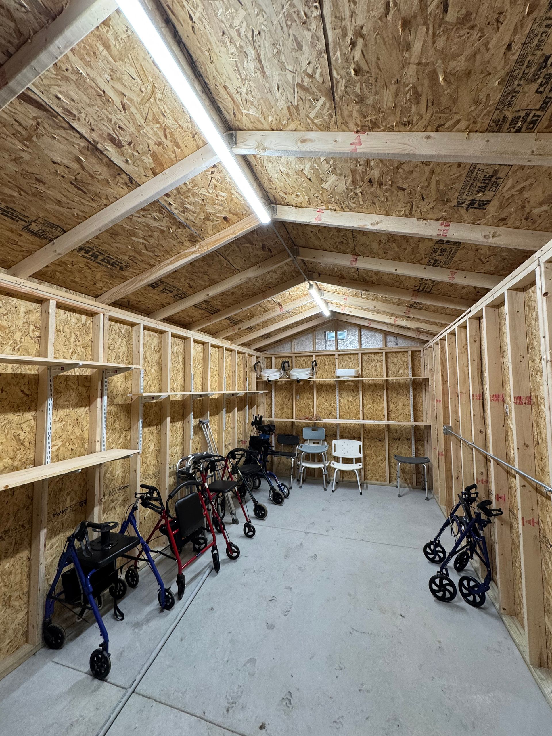 Interior of a storage shed with multiple walkers lined along the walls. Wooden shelves and supports are visible.