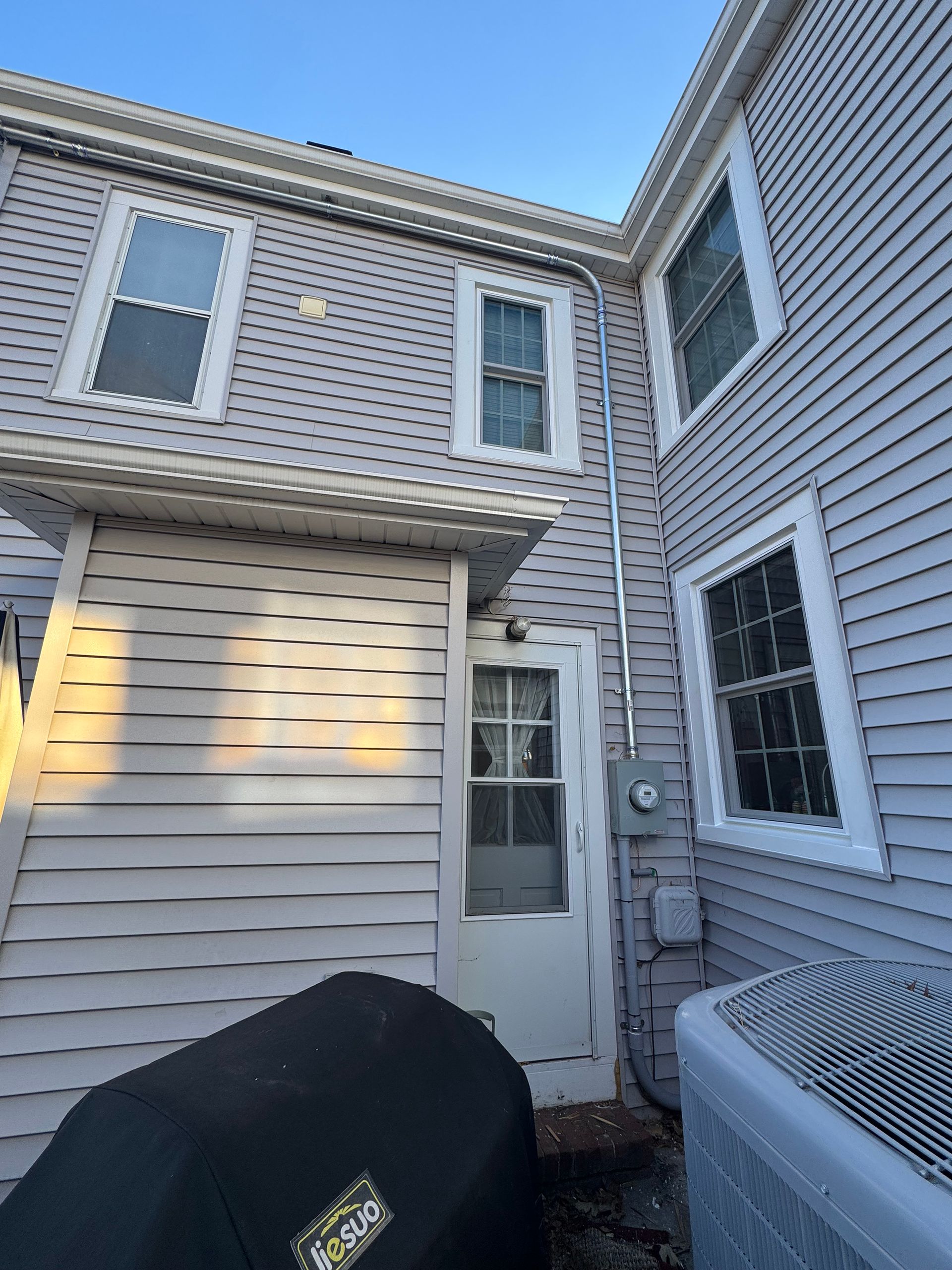 Exterior view of a light gray house with white trim windows and a covered doorway.