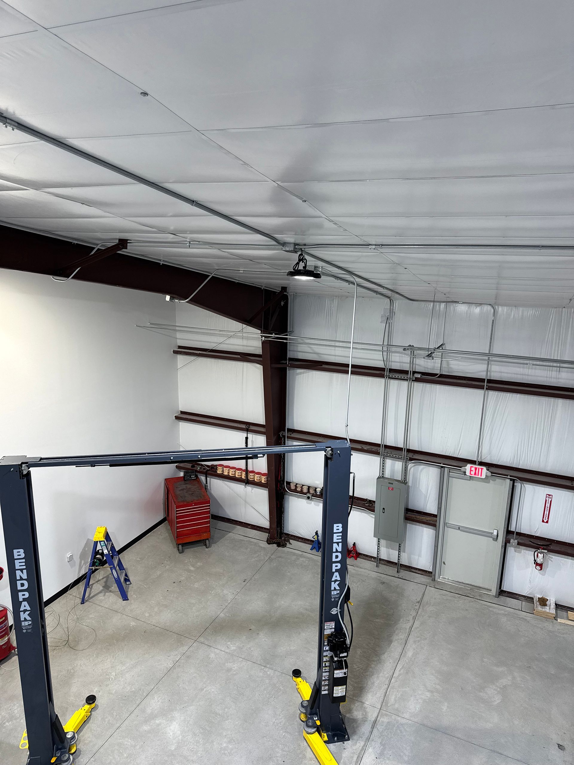 A car repair shop interior with a vehicle lift, electrical conduits, and a closed door.