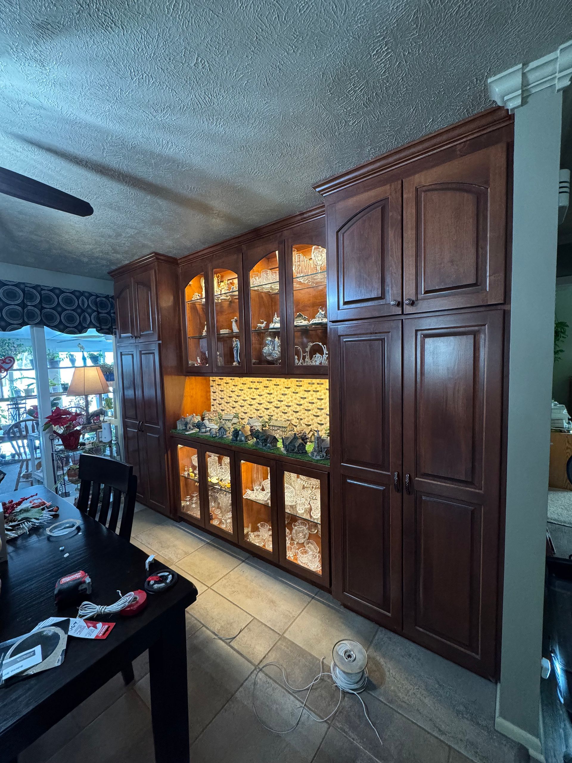 Dark wood cabinets in a dining room, some with glass doors and interior lighting. A dining table is in foreground.