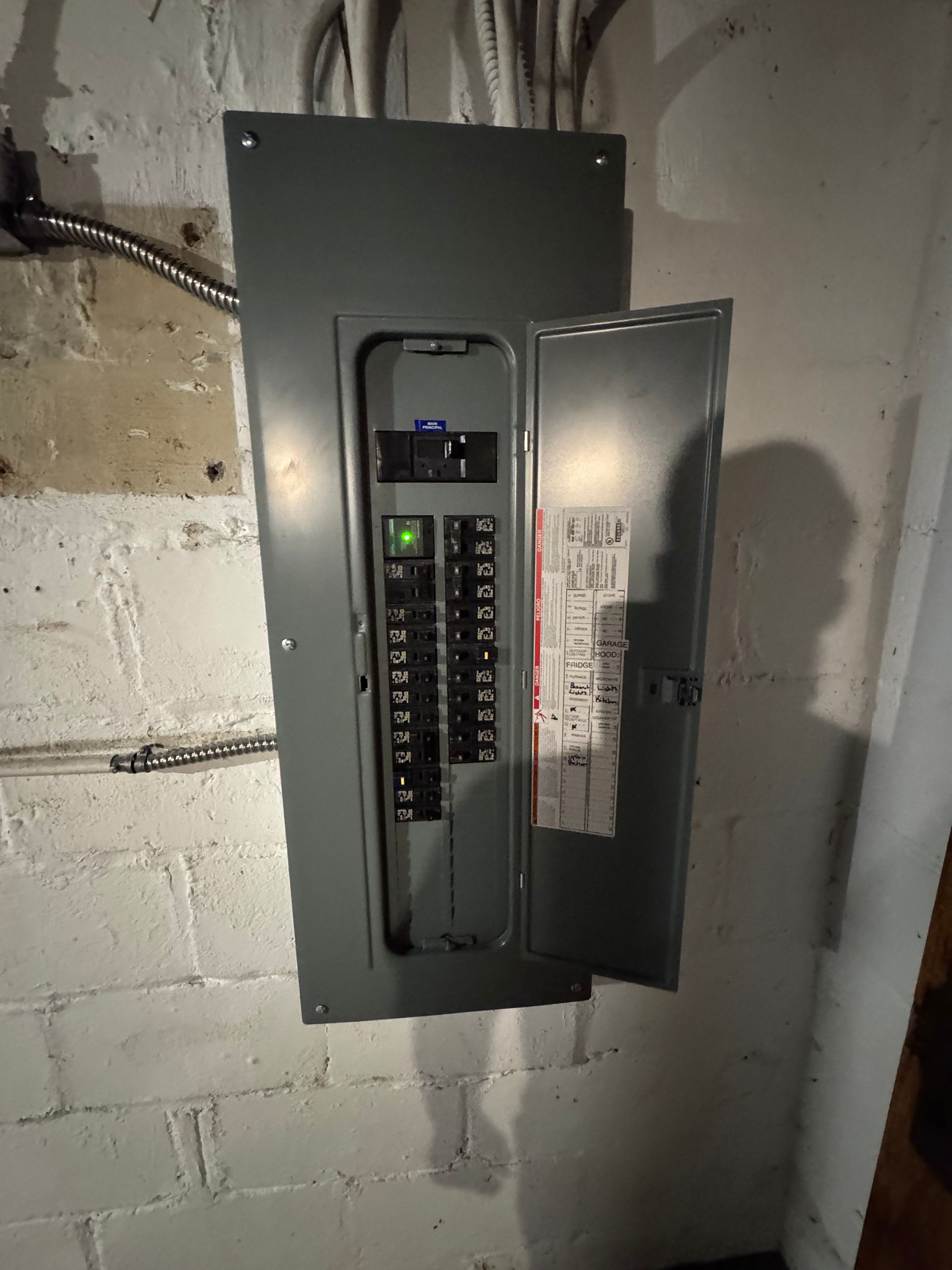 Electrical panel with the door open, mounted on a white brick wall.