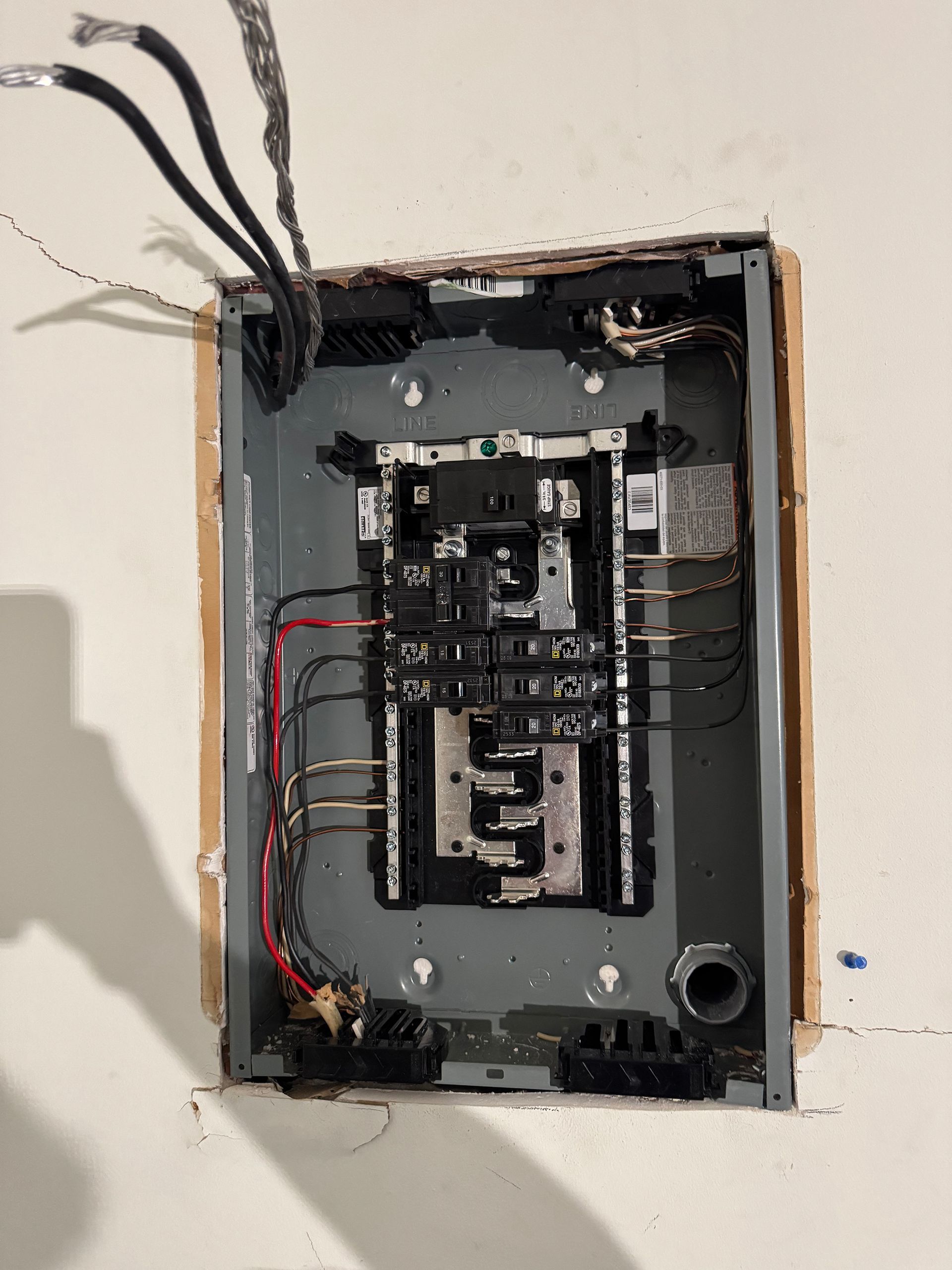Open electrical panel with exposed wires on a white wall.