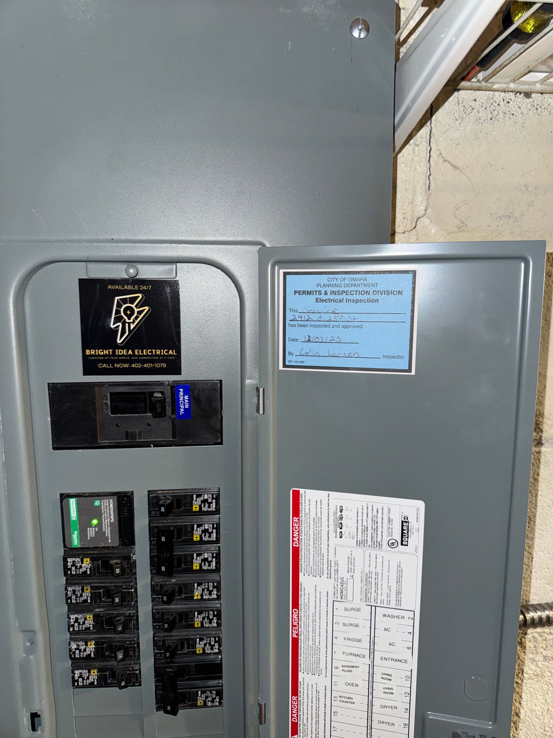 Open electrical panel with circuit breakers, labels, and a sticker.
