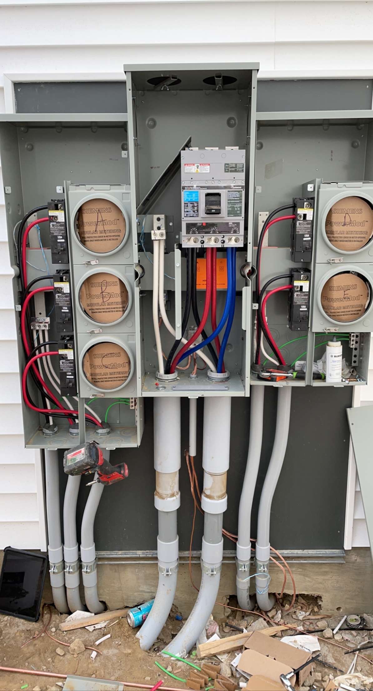 Electrical meter box with three meter sockets and conduit, mounted on a white wall; exposed wiring.