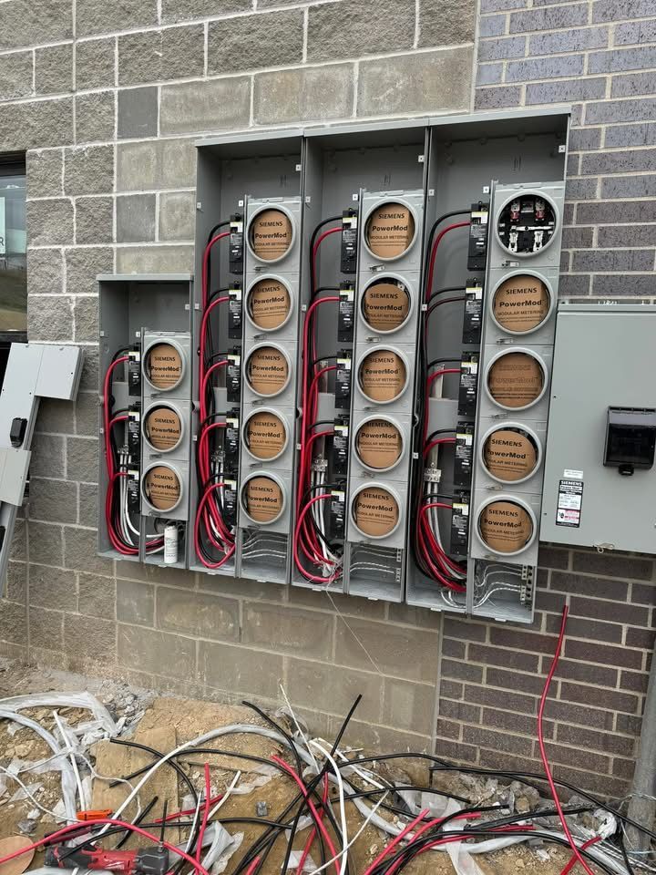 Electrical meters installed on an exterior brick wall, with exposed red and black wiring.