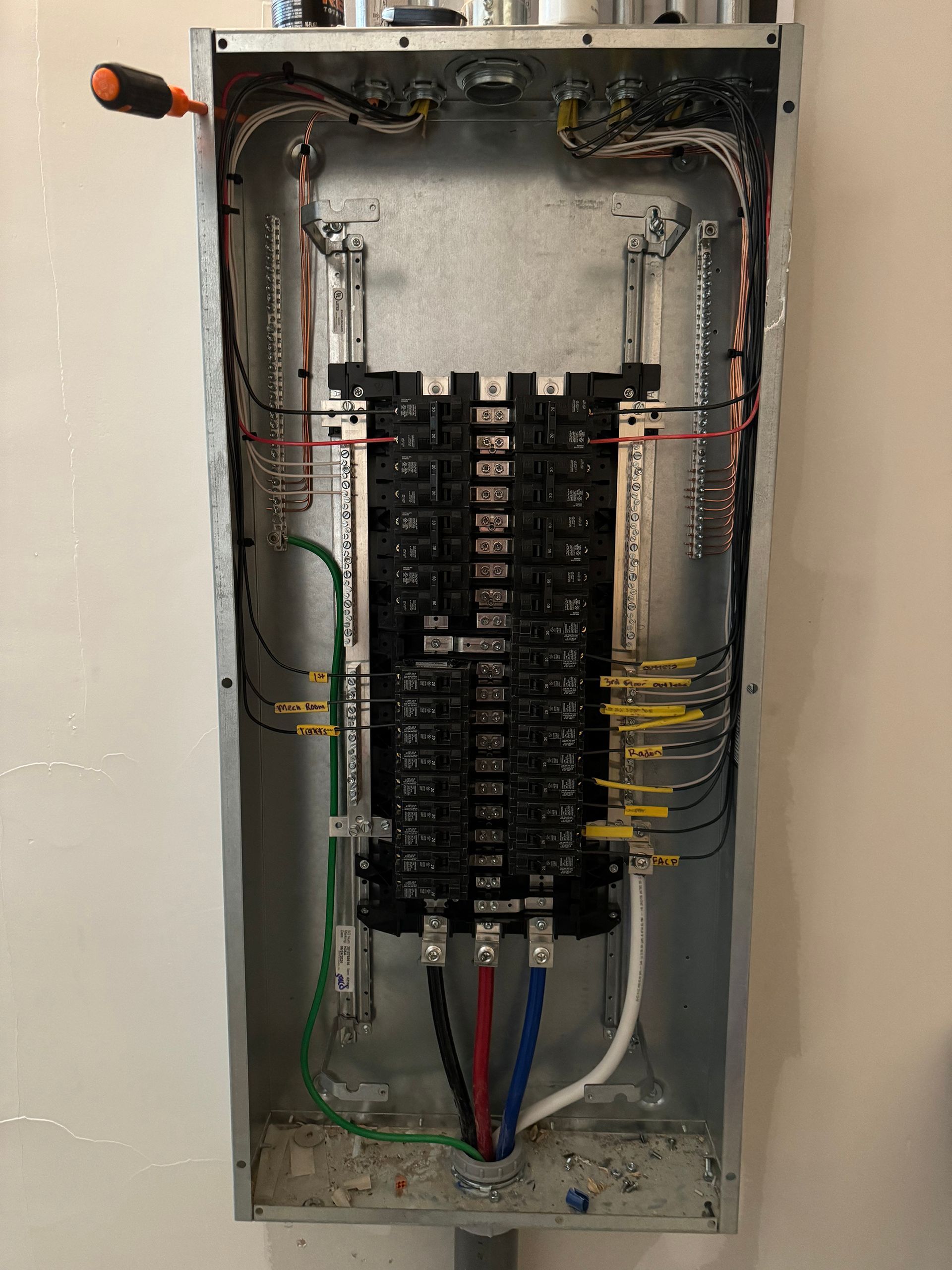 Open electrical panel with wires and circuit breakers. Gray metal box mounted on a wall.