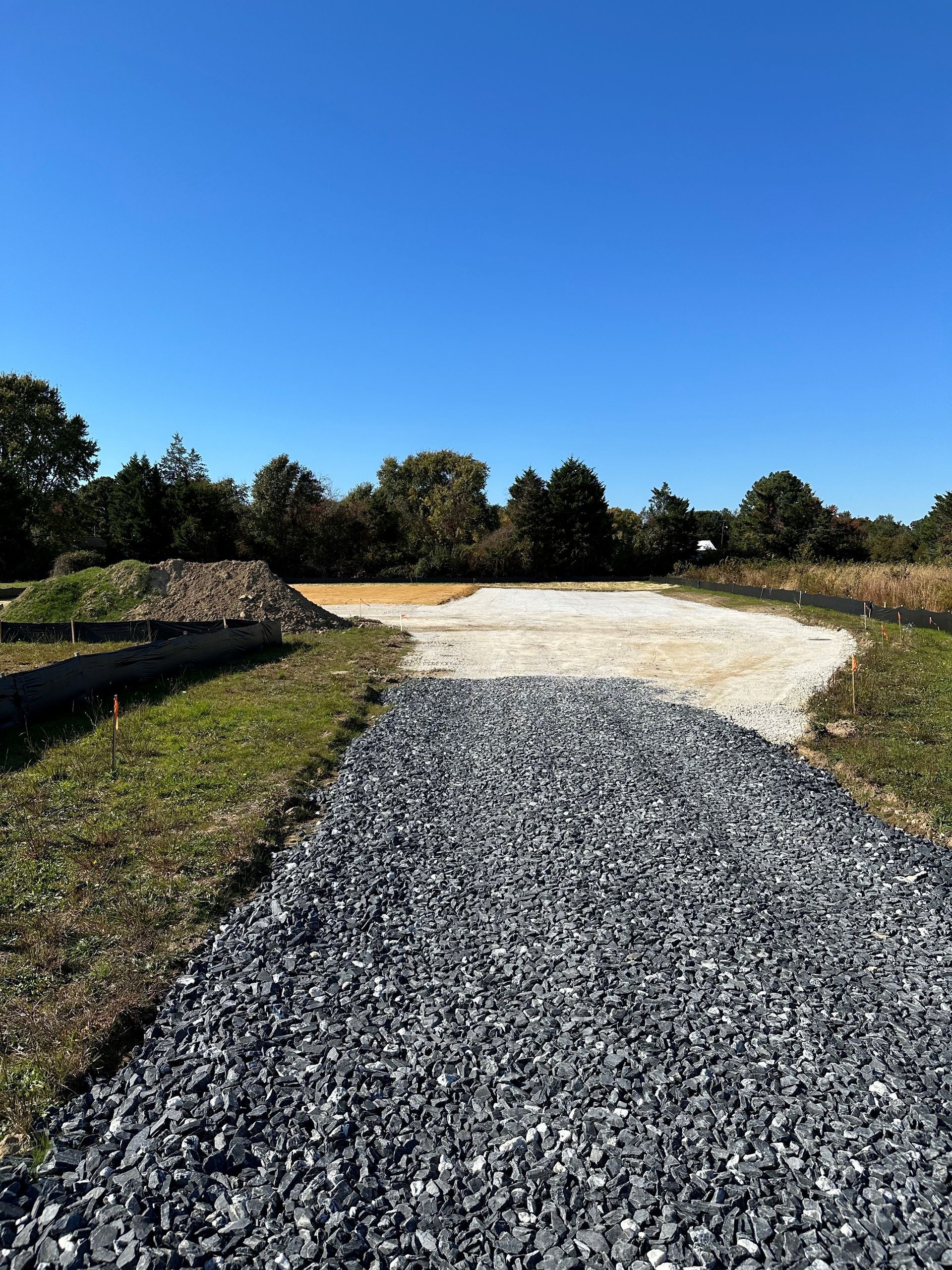 A gravel road going through a grassy field with trees in the background