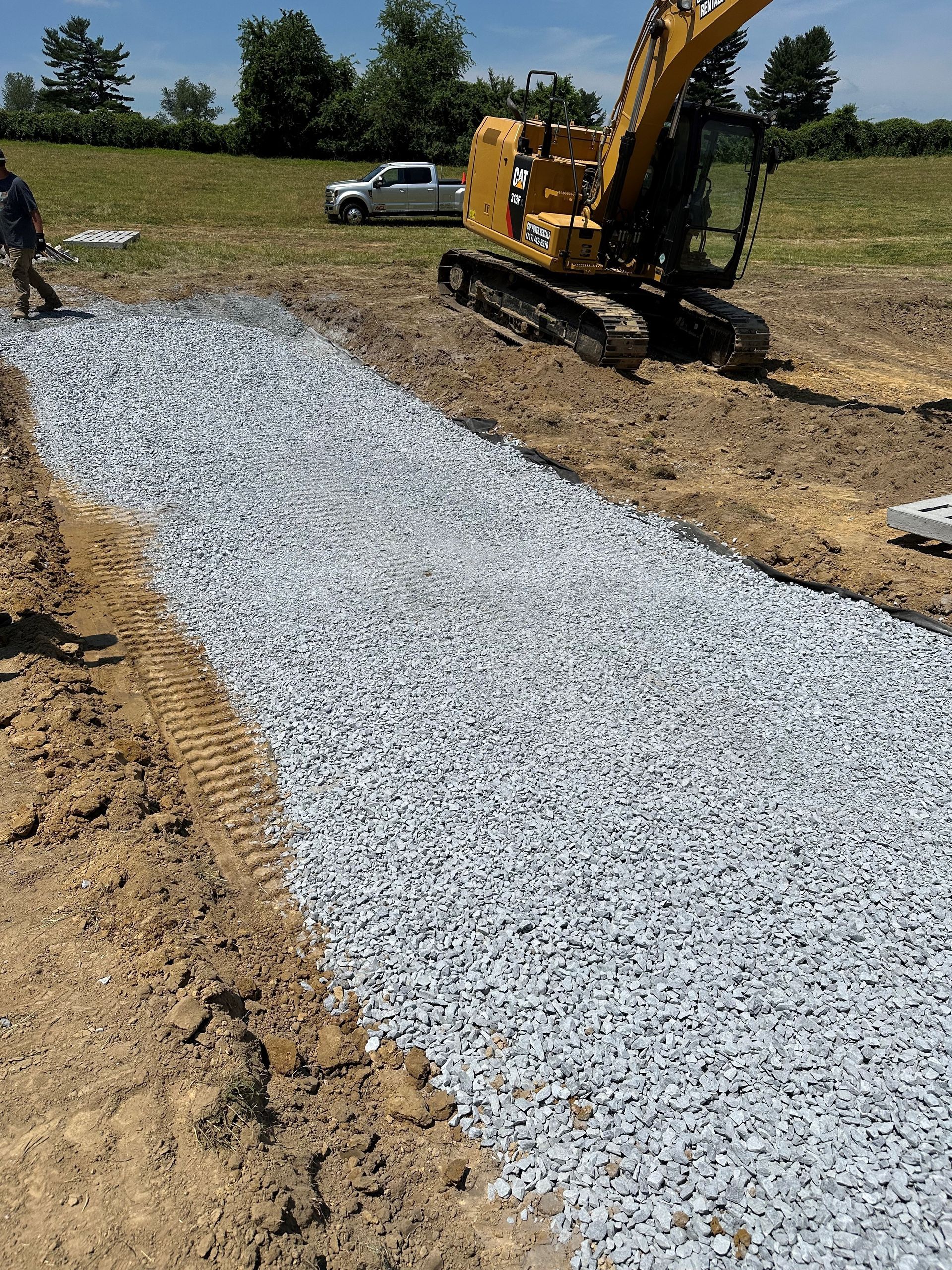 A yellow excavator is laying gravel in a field