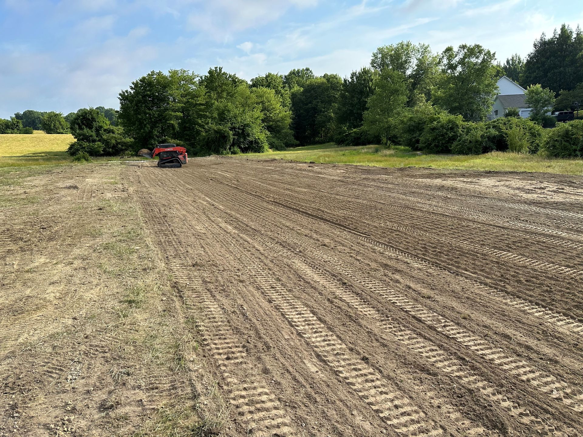 A red tractor is plowing a field with trees in the background