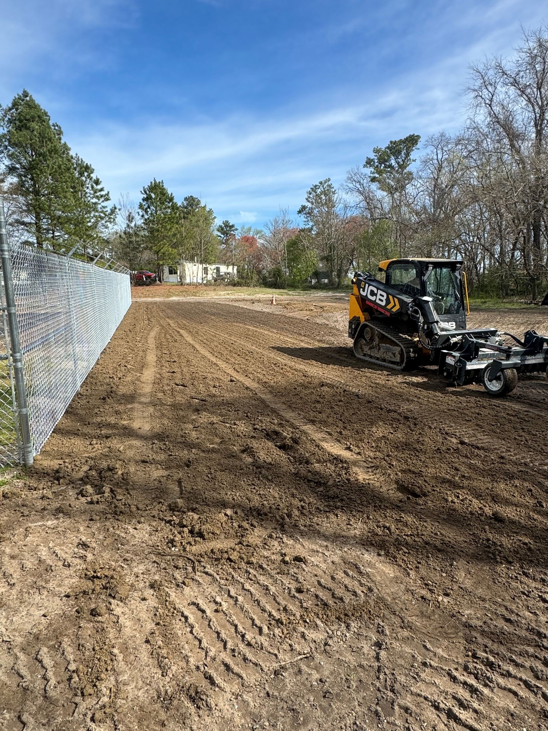 A bulldozer is driving down a dirt road next to a fence