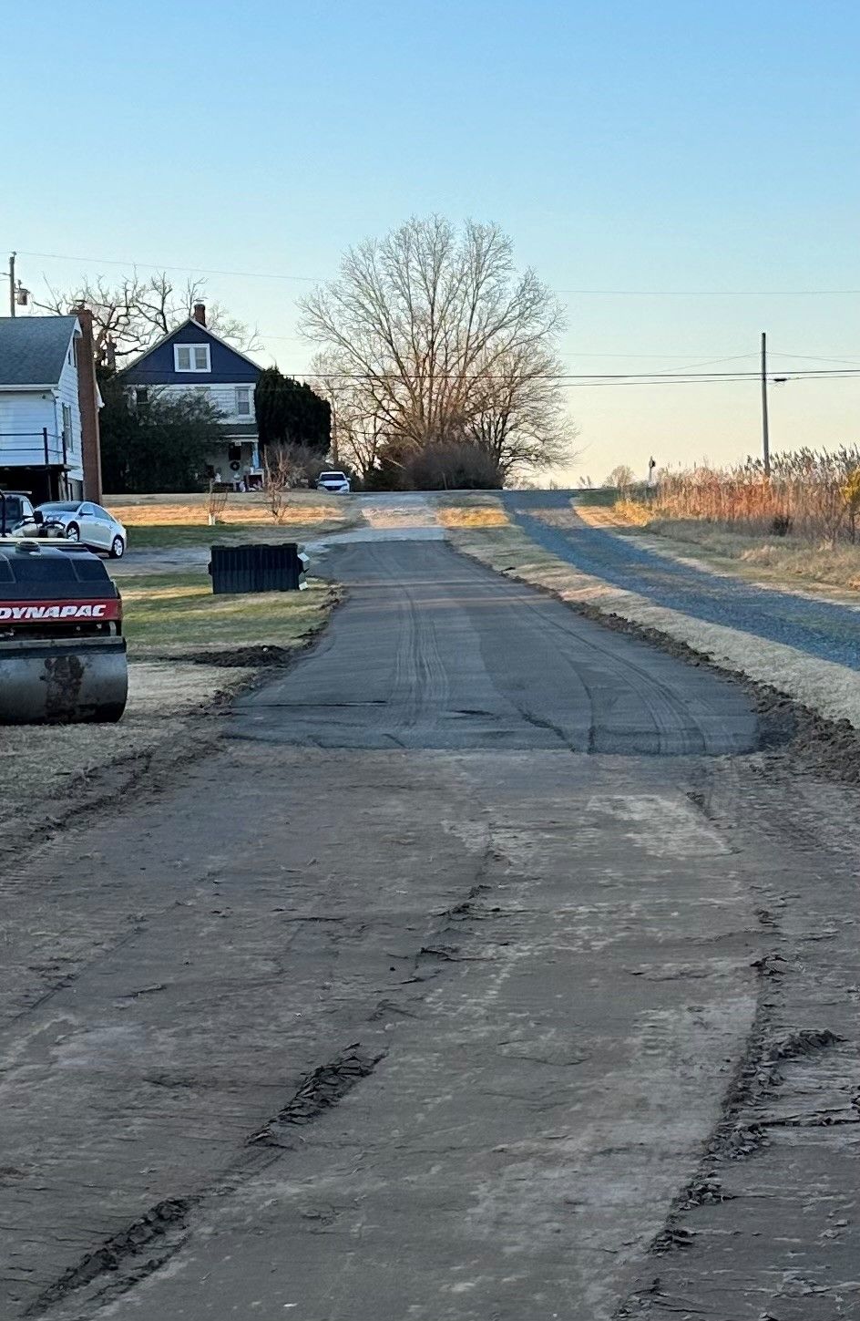 A road is being paved in a rural area with a house in the background