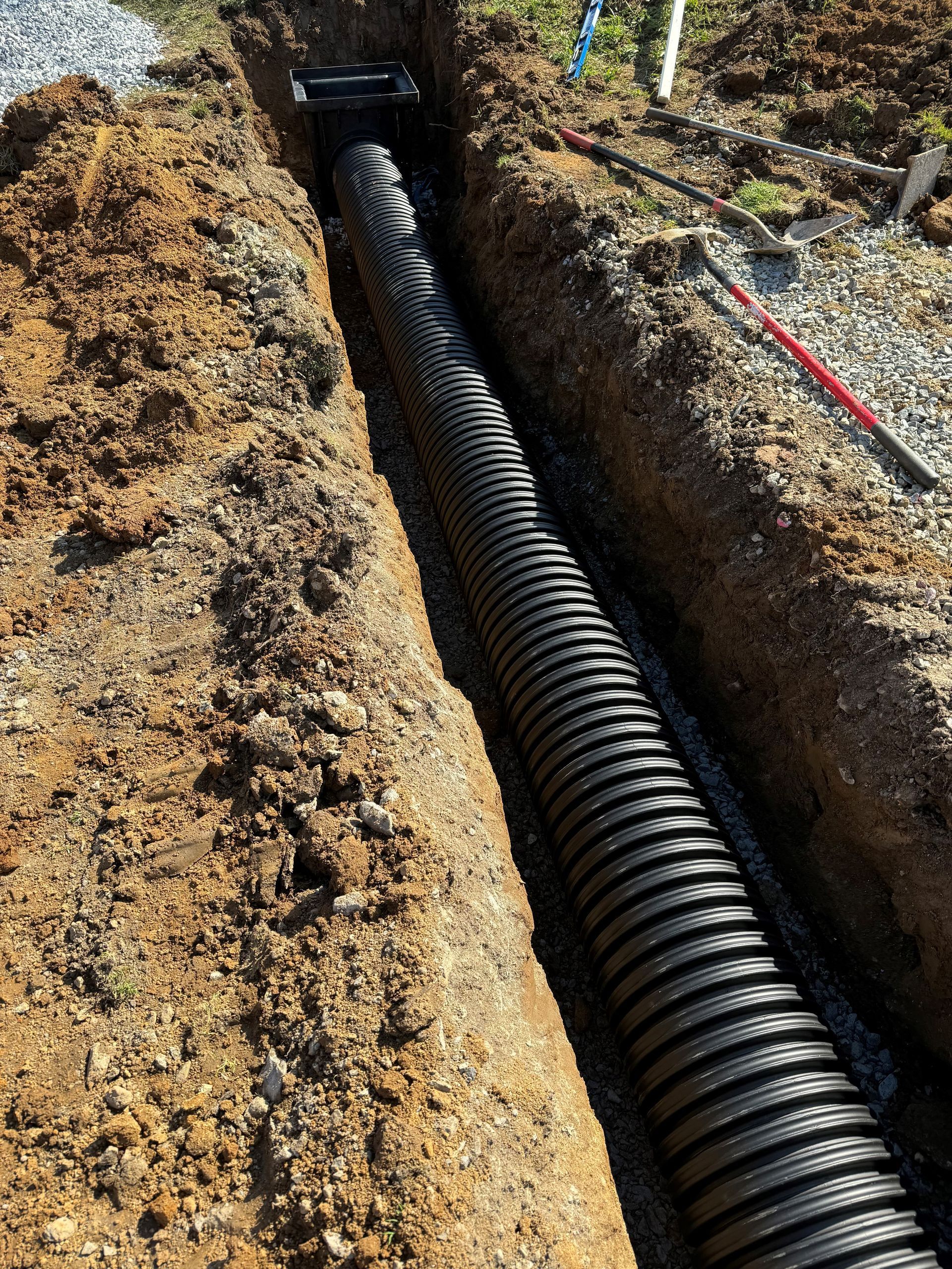A large black pipe is being installed in the dirt