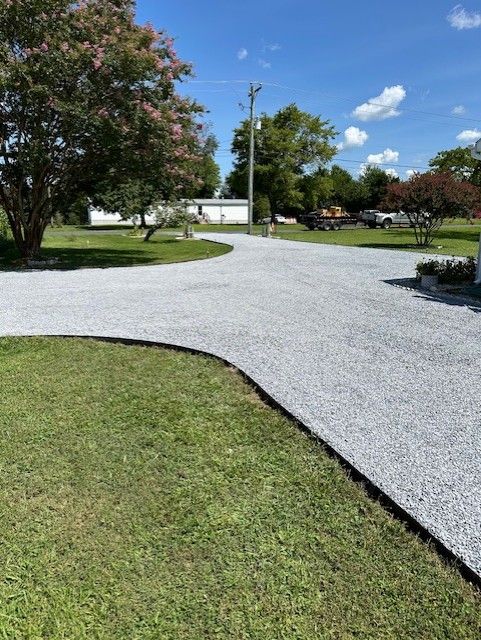 A gravel driveway going through a lush green field