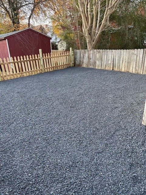 A gravel driveway with a wooden fence and a red barn in the background