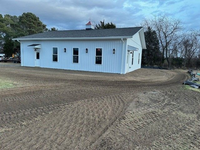 A white house with a black roof is sitting in the middle of a dirt field