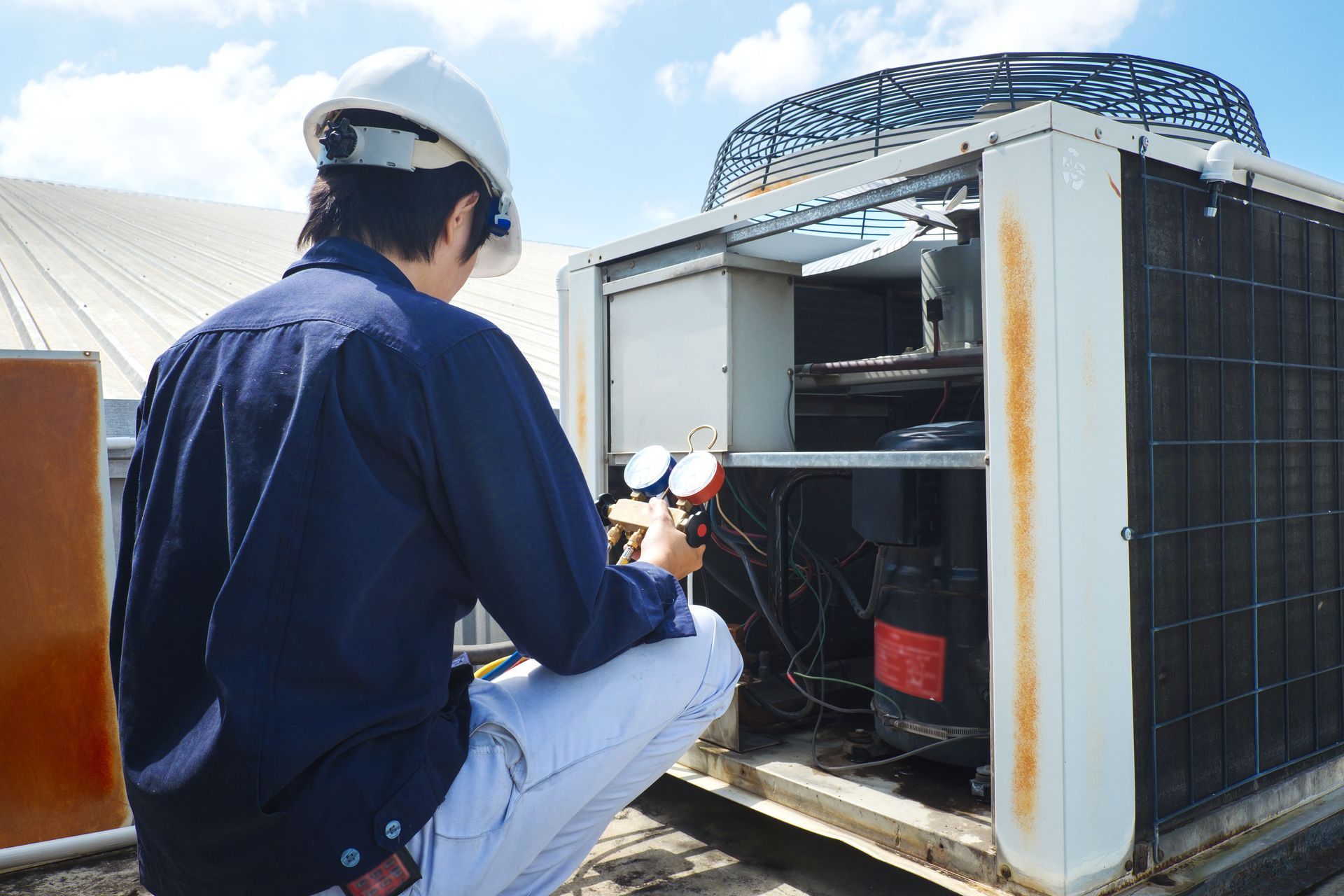 A man is kneeling down in front of an air conditioner.