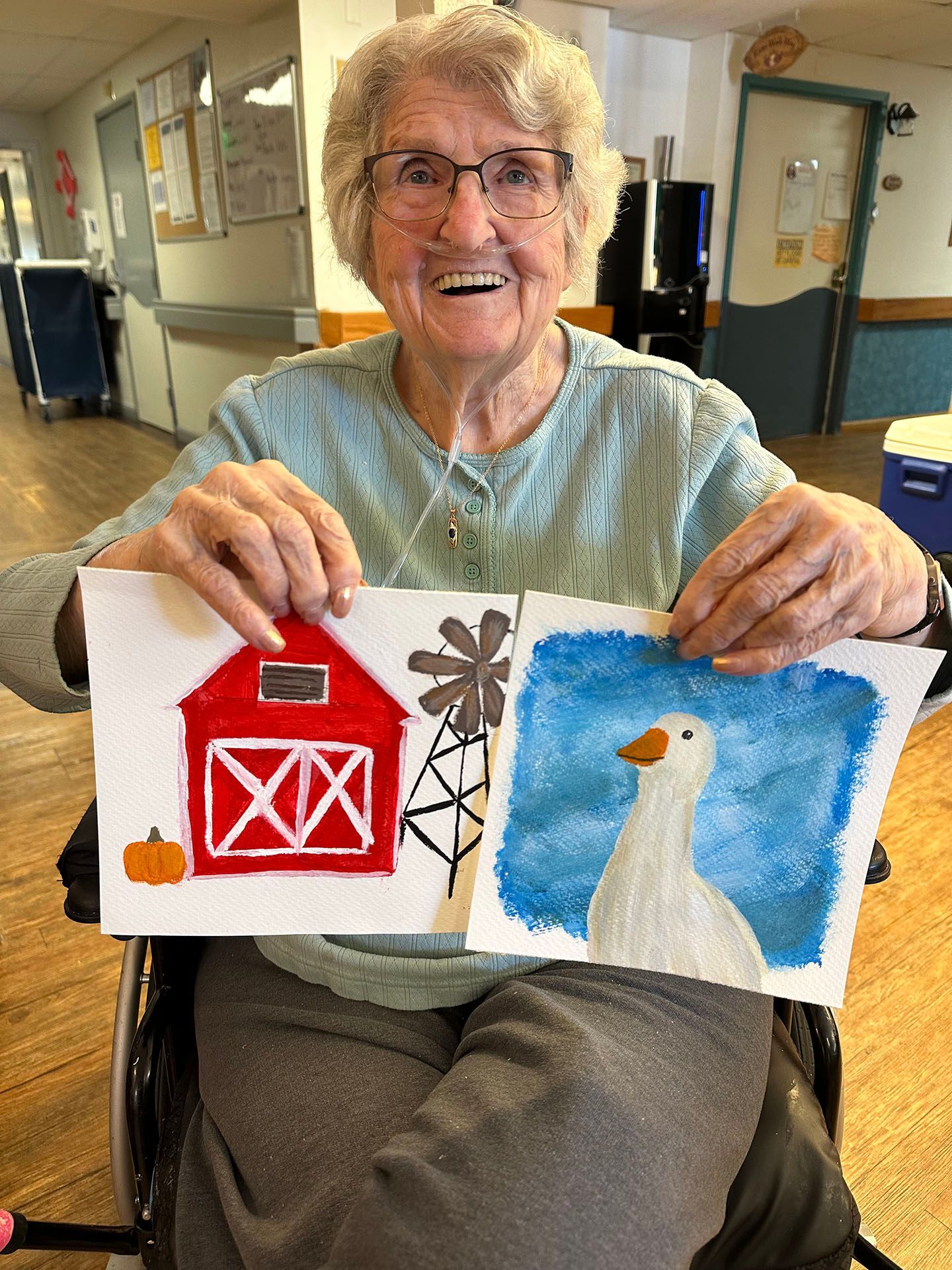 an elderly woman in a wheelchair is holding a painting of a barn and a duck