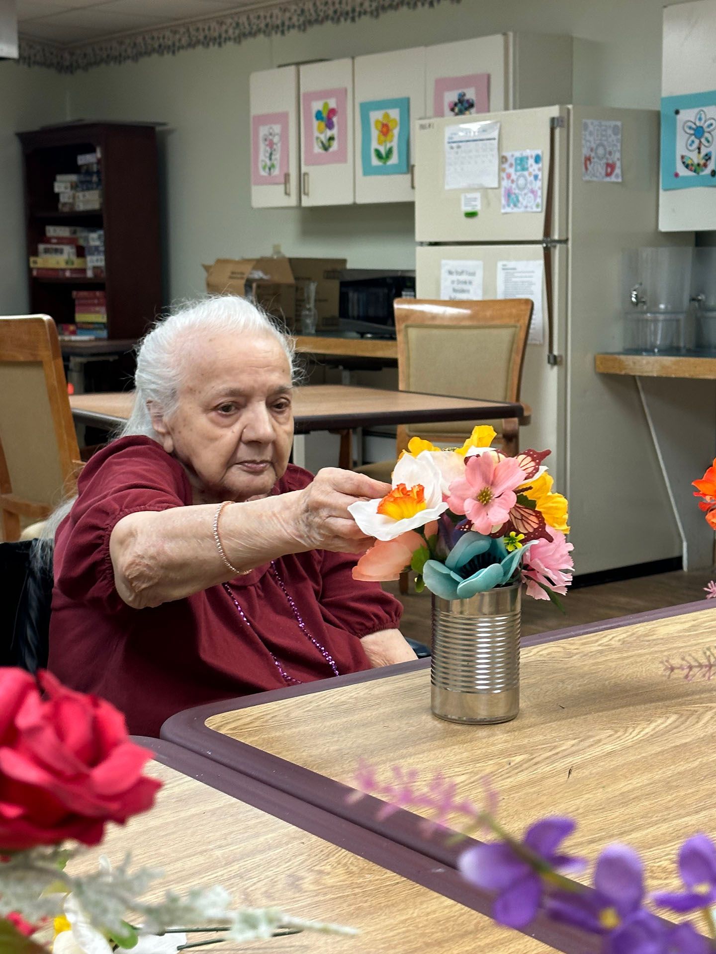 an elderly woman is sitting at a table with a vase of flowers