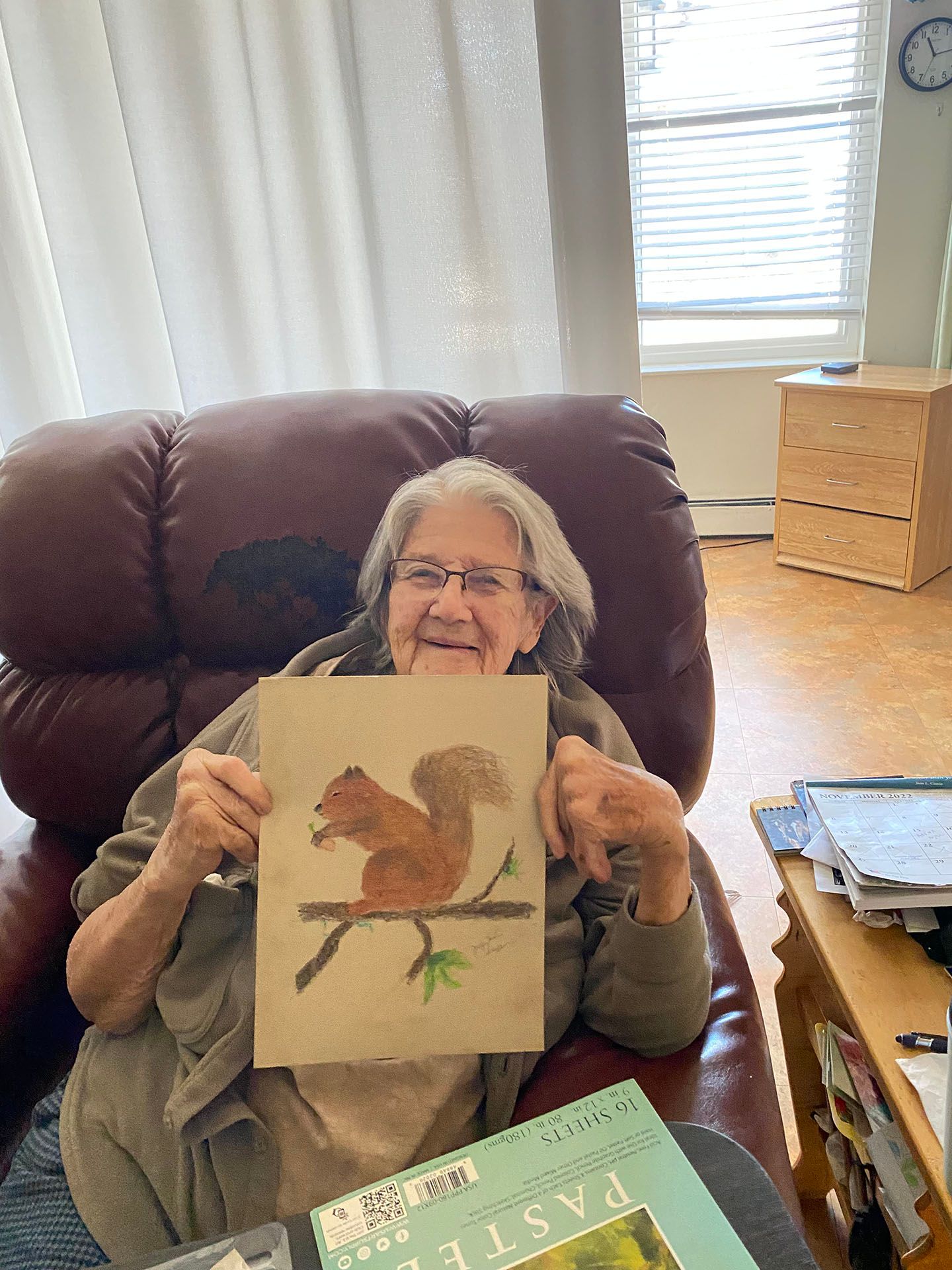 an elderly woman is sitting in a chair holding a painting of a squirrel