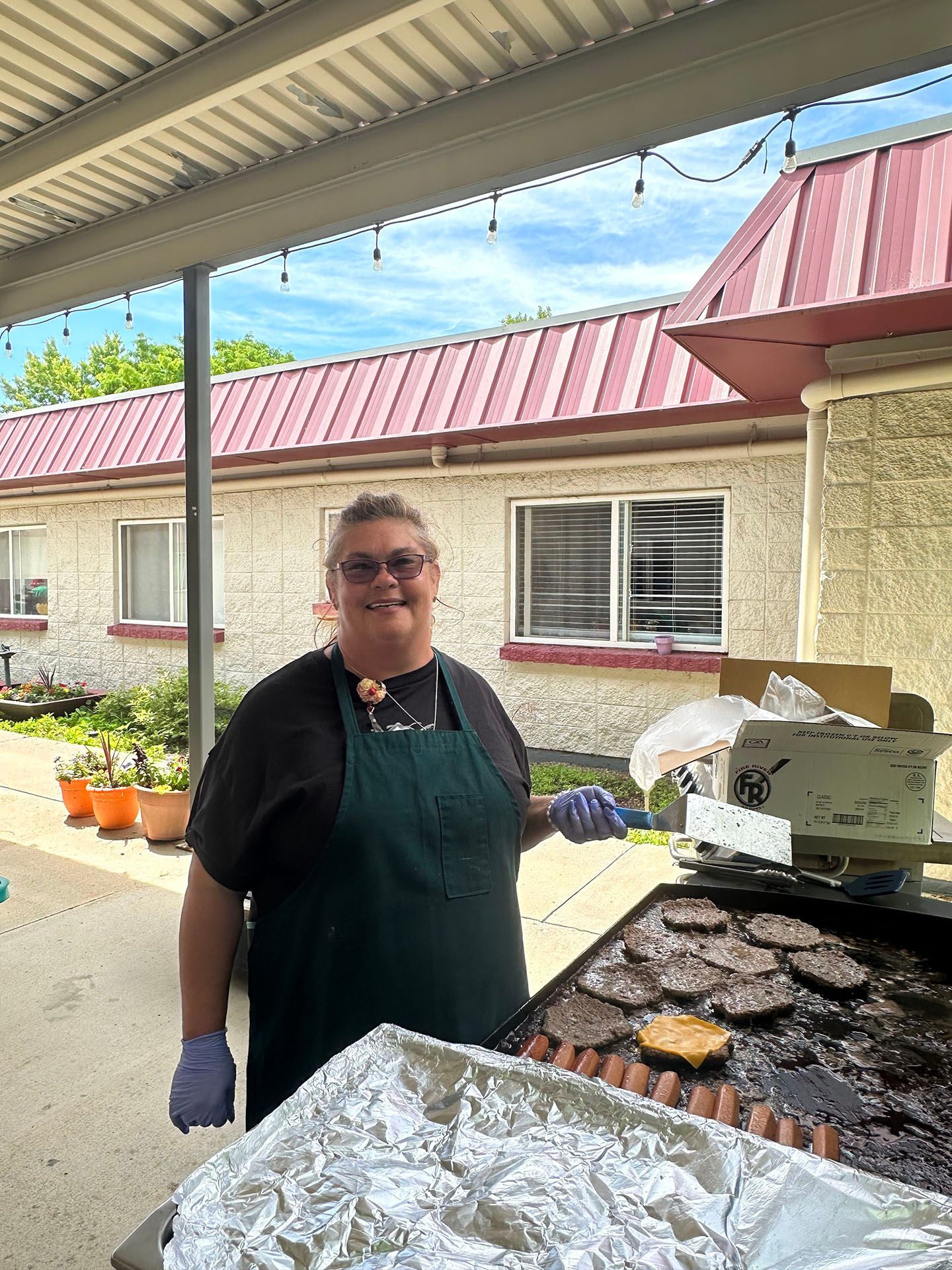 a woman is standing in front of a grill with hamburgers on it