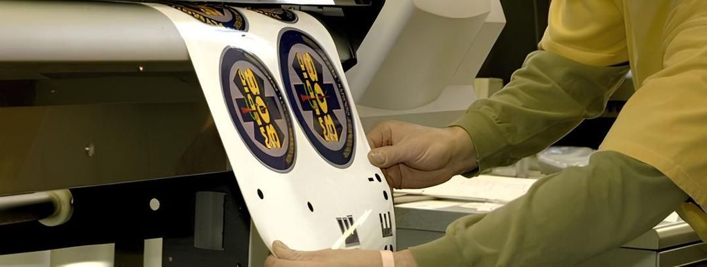 A person holding a printed sheet with round stickers from a printing machine.