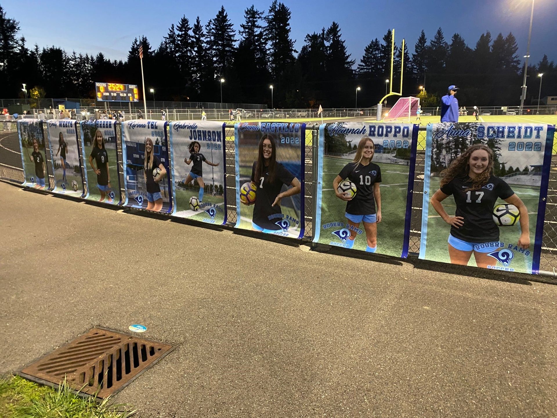 Banners with soccer players' photos on a track. Blue, green, and white with a forest background.