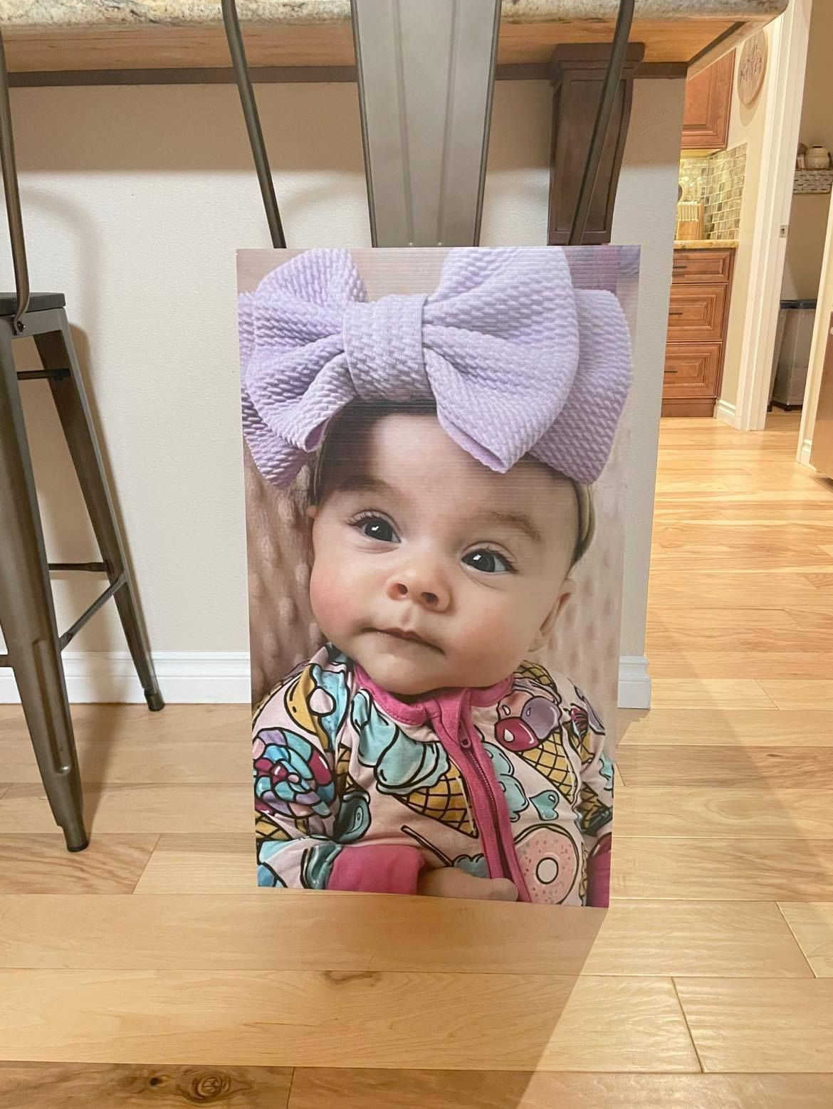 A baby wearing a light purple bow in front of a wooden background.