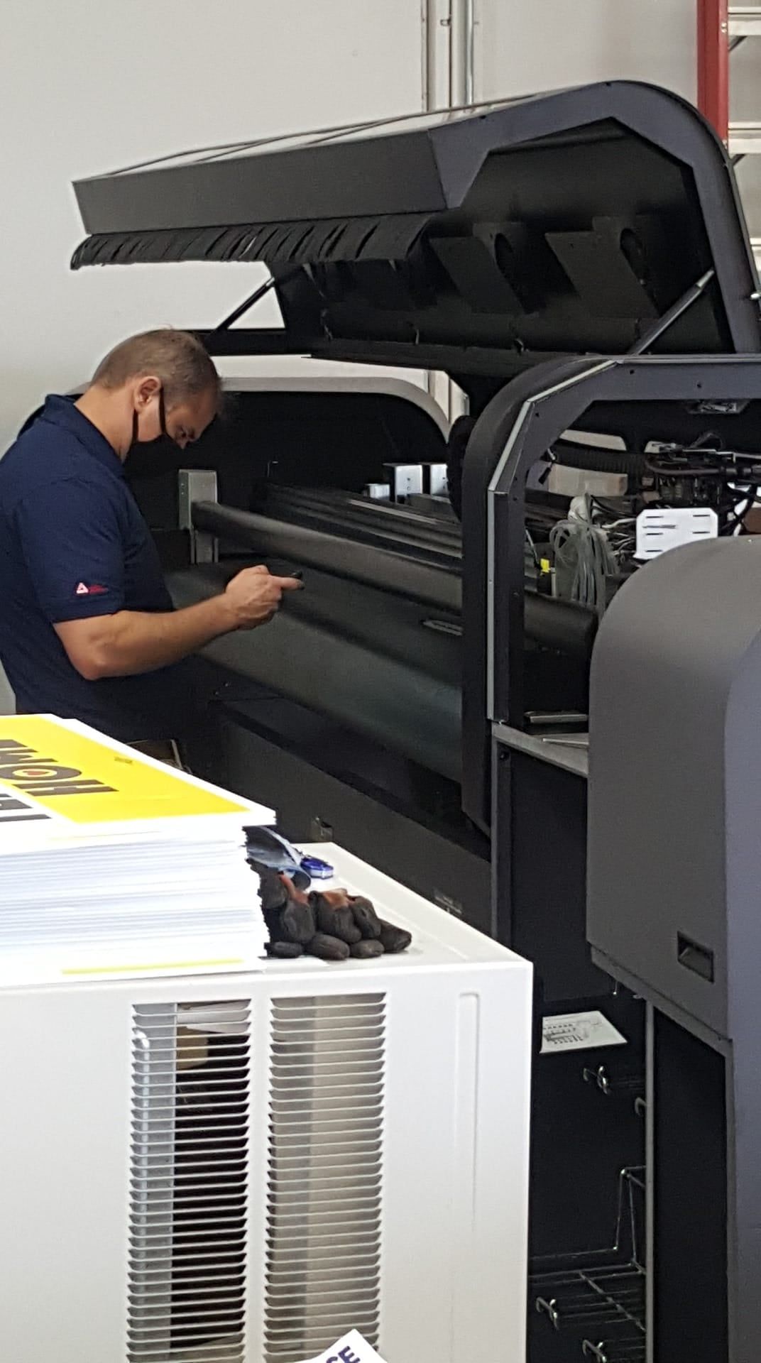 Man in mask working on a large printing machine in a print shop.