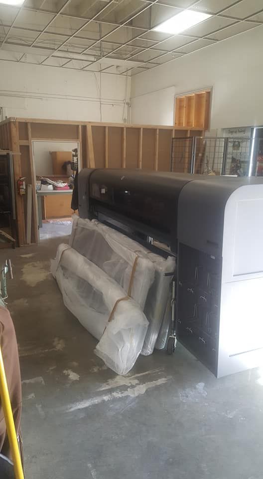 Large-format printer in a workshop, near wrapped panels. Interior shot with neutral-toned walls and exposed ceiling.