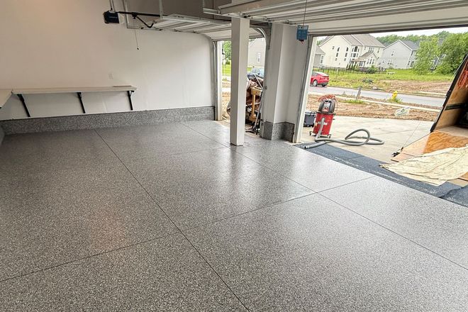 Empty speckled garage interior with open doorway to a driveway and street outside