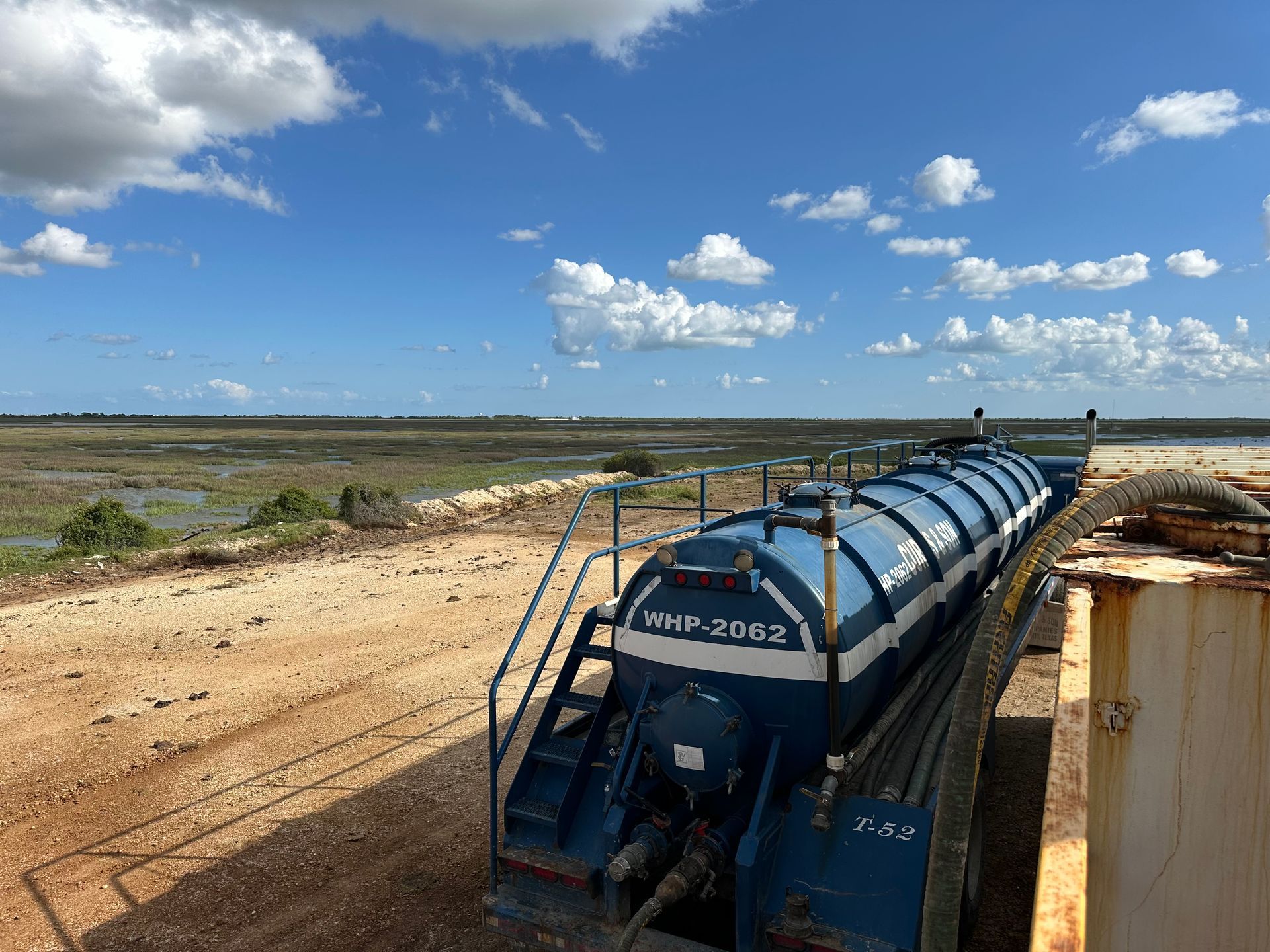 A large blue and white tanker truck is parked on the side of a dirt road.