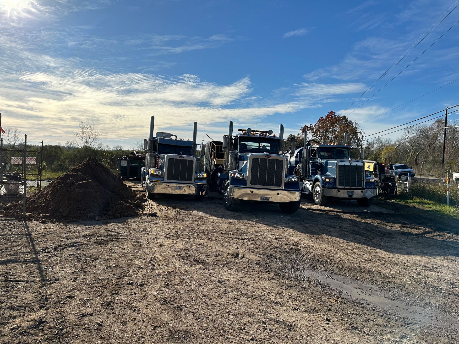 Three semi trucks are parked on the side of a dirt road.