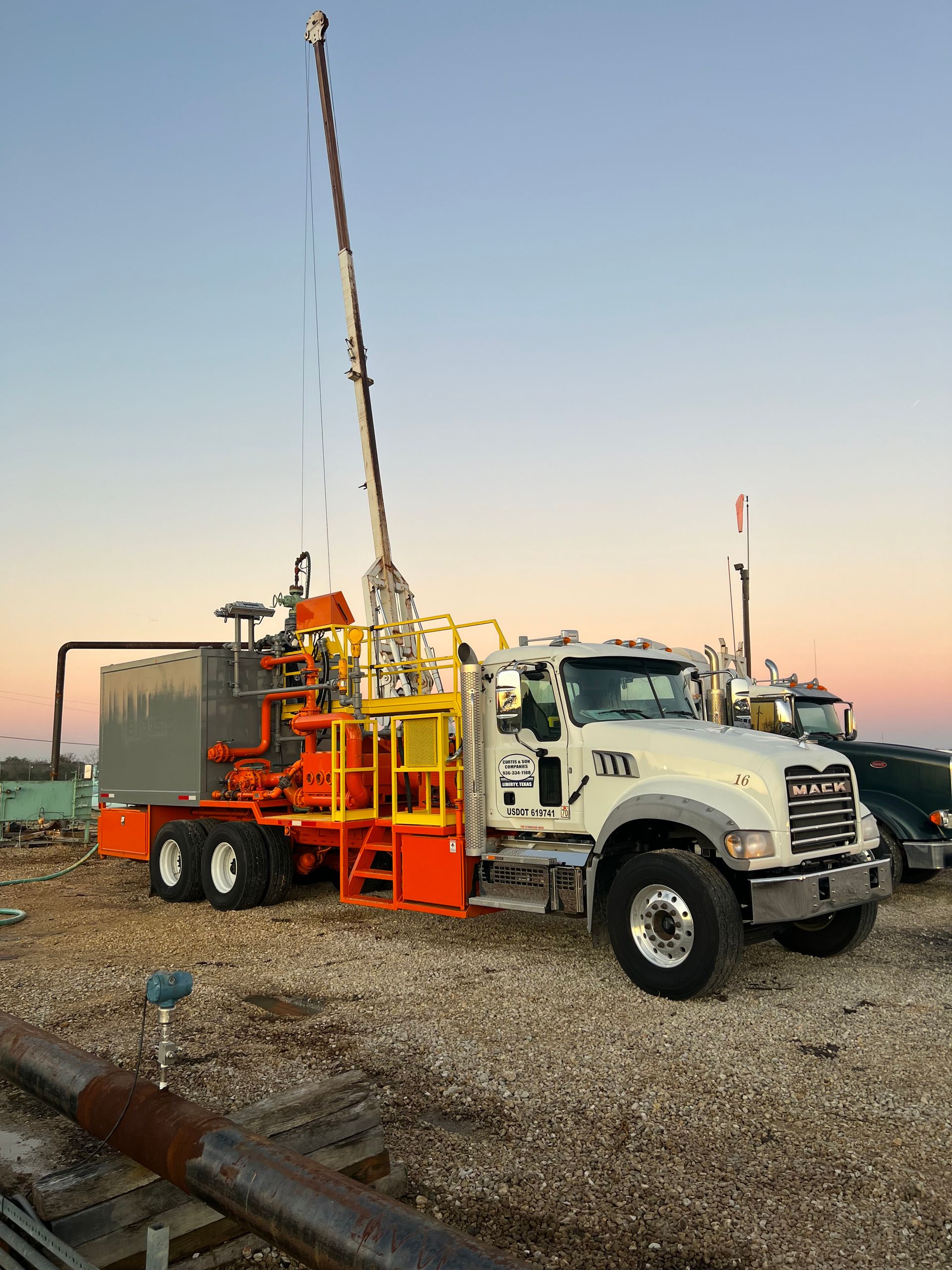 A truck with a crane attached to it is parked in a gravel lot.