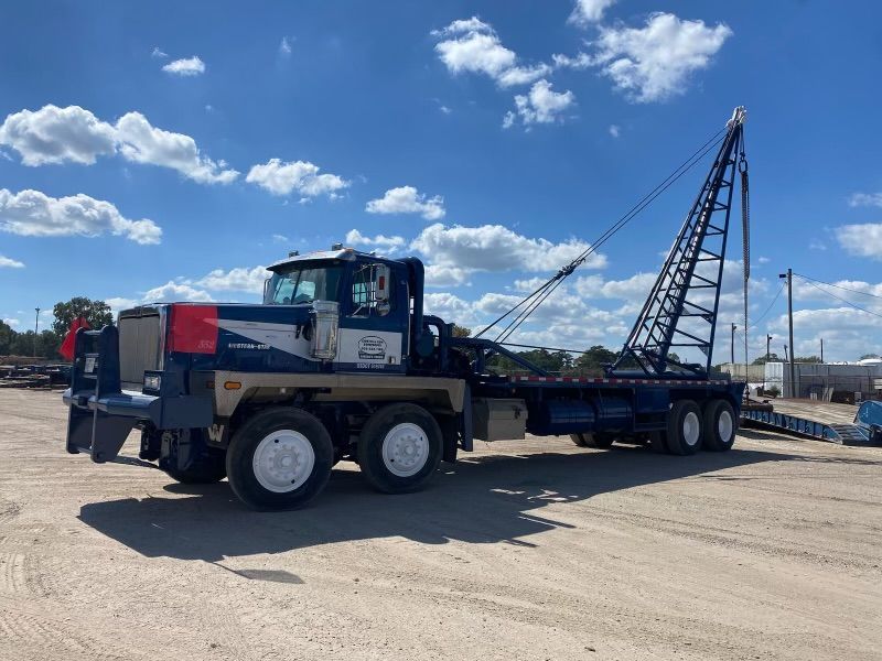 A tow truck with a crane attached to it is parked in a dirt lot.